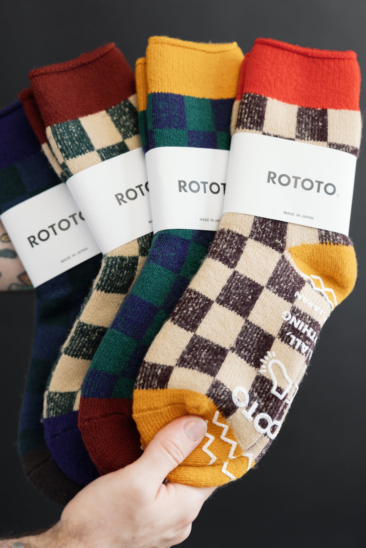 Close-up front view of checkered patterned socks in red, yellow, and dark green held by a hand.