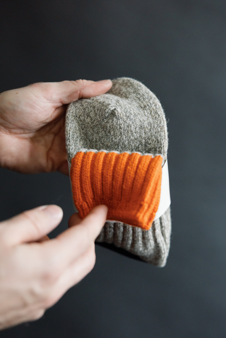 Close-up of hand holding Rototo R1536 merino wool rug sock, orange ribbed cuff detail, front view