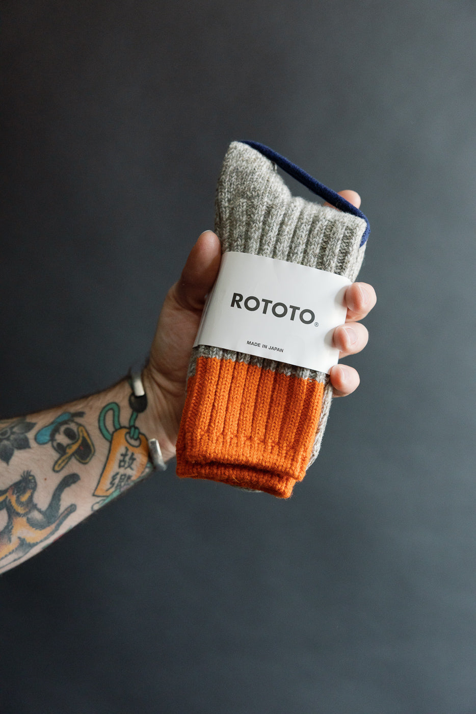 Close-up of hand holding Rototo R1536 Merino Wool Rug Socks, orange and grey, front view.