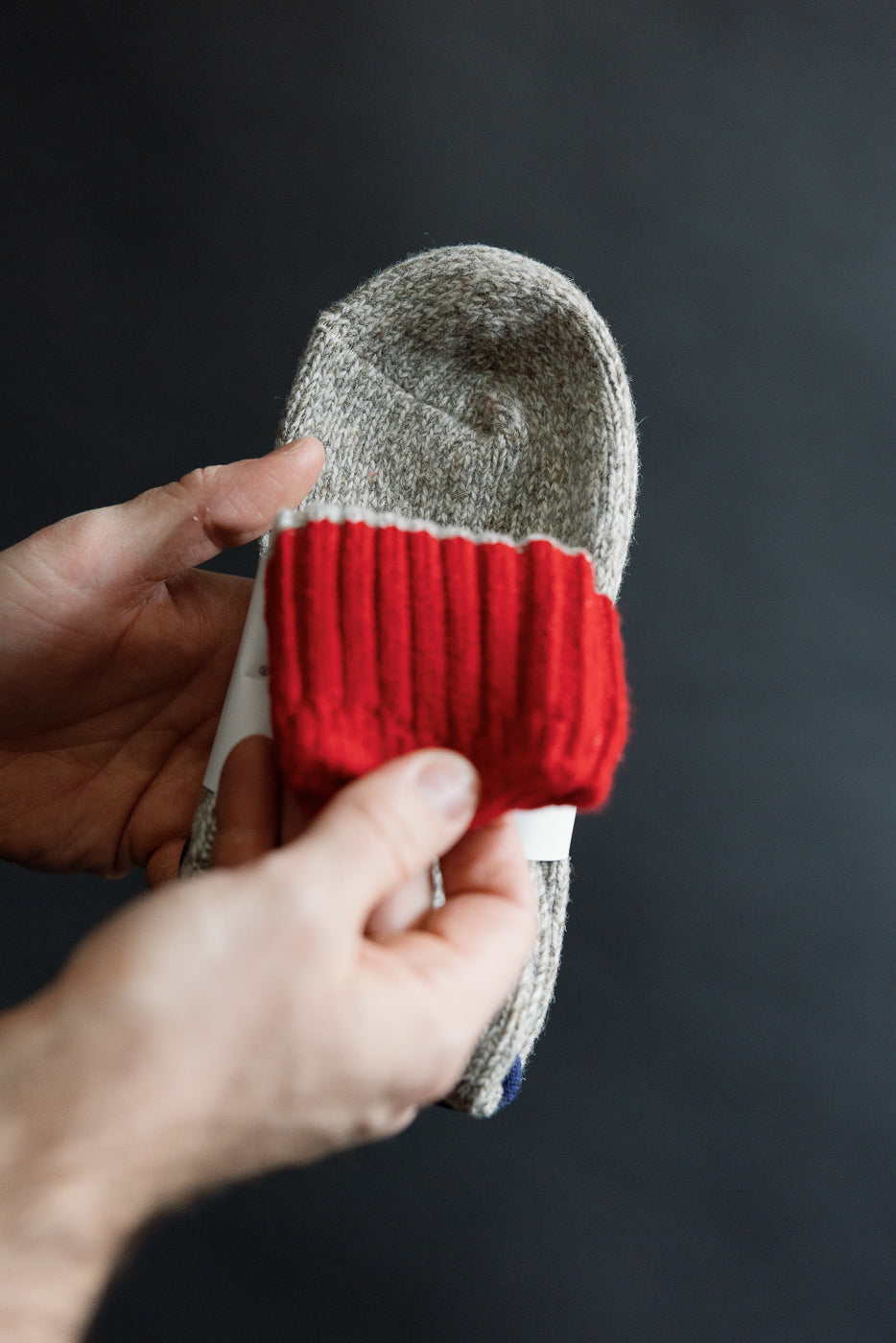 Close-up of hands holding Rototo Merino Wool Rug Socks in grey and red, showing cuff detail.
