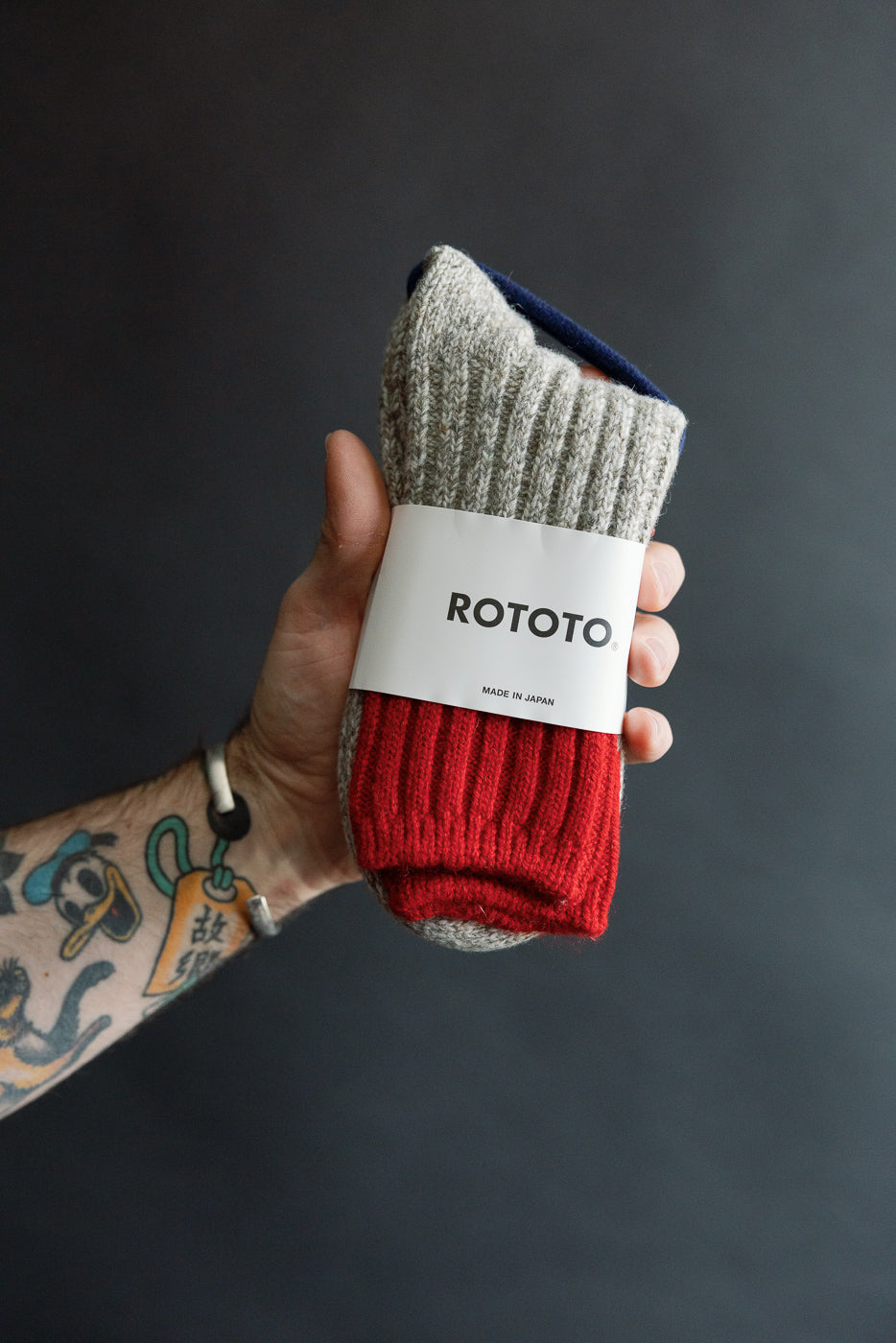 Close-up of hand holding Rototo merino wool rug socks, red and grey, front view, Dant shop.