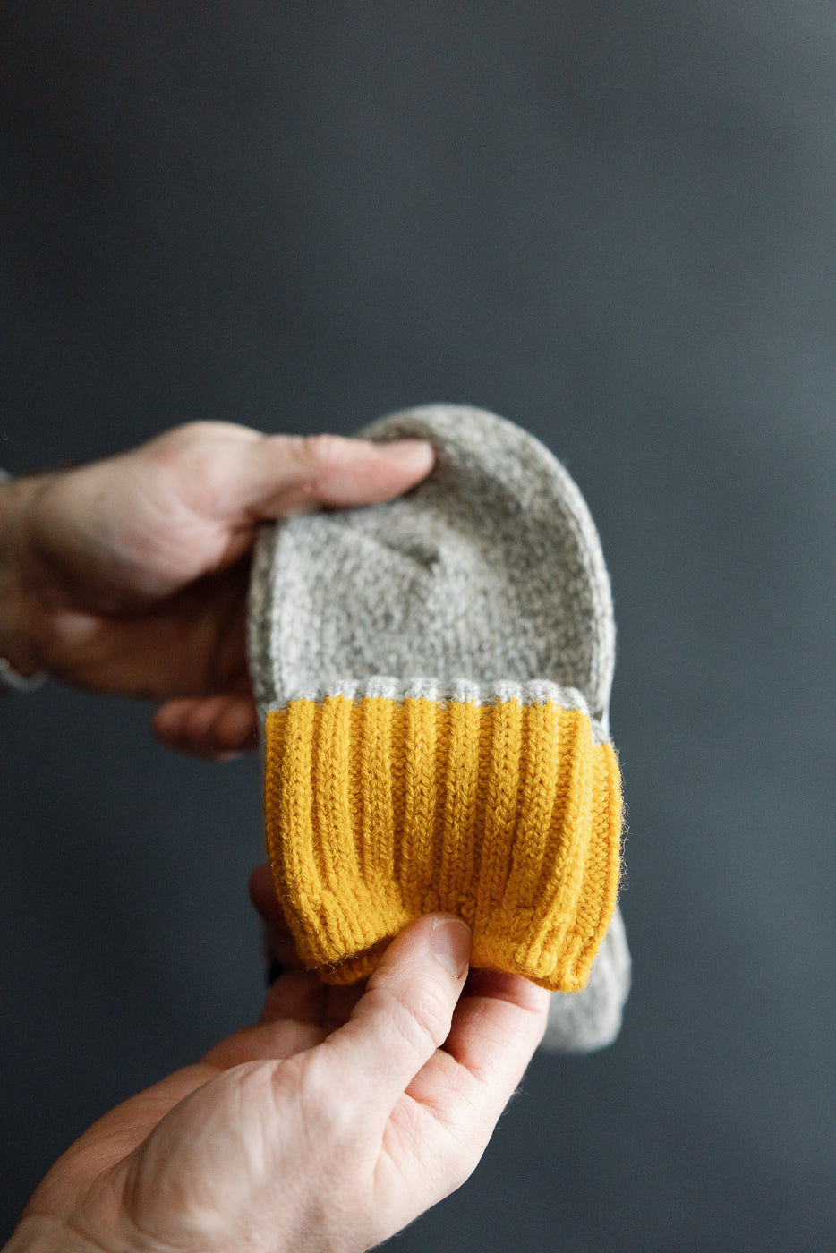 Close-up of hand holding Rototo R1536 merino wool rug sock, showing yellow ribbed cuff detail, front view.