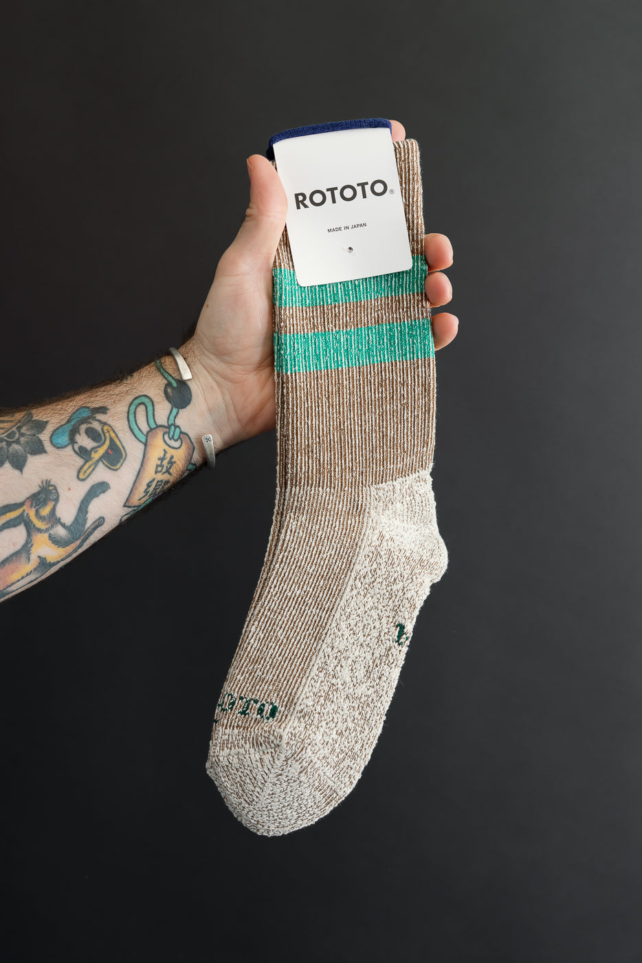 Close-up of the front of a beige ribbed Rototo sock with green stripes and logo detail.