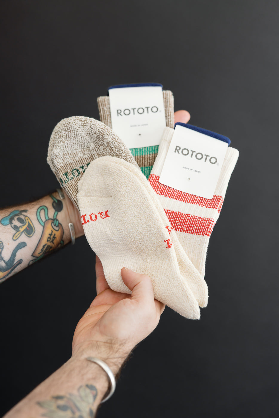 Close-up of a male's hands holding three pairs of ROTOTO socks with texture and tags.
