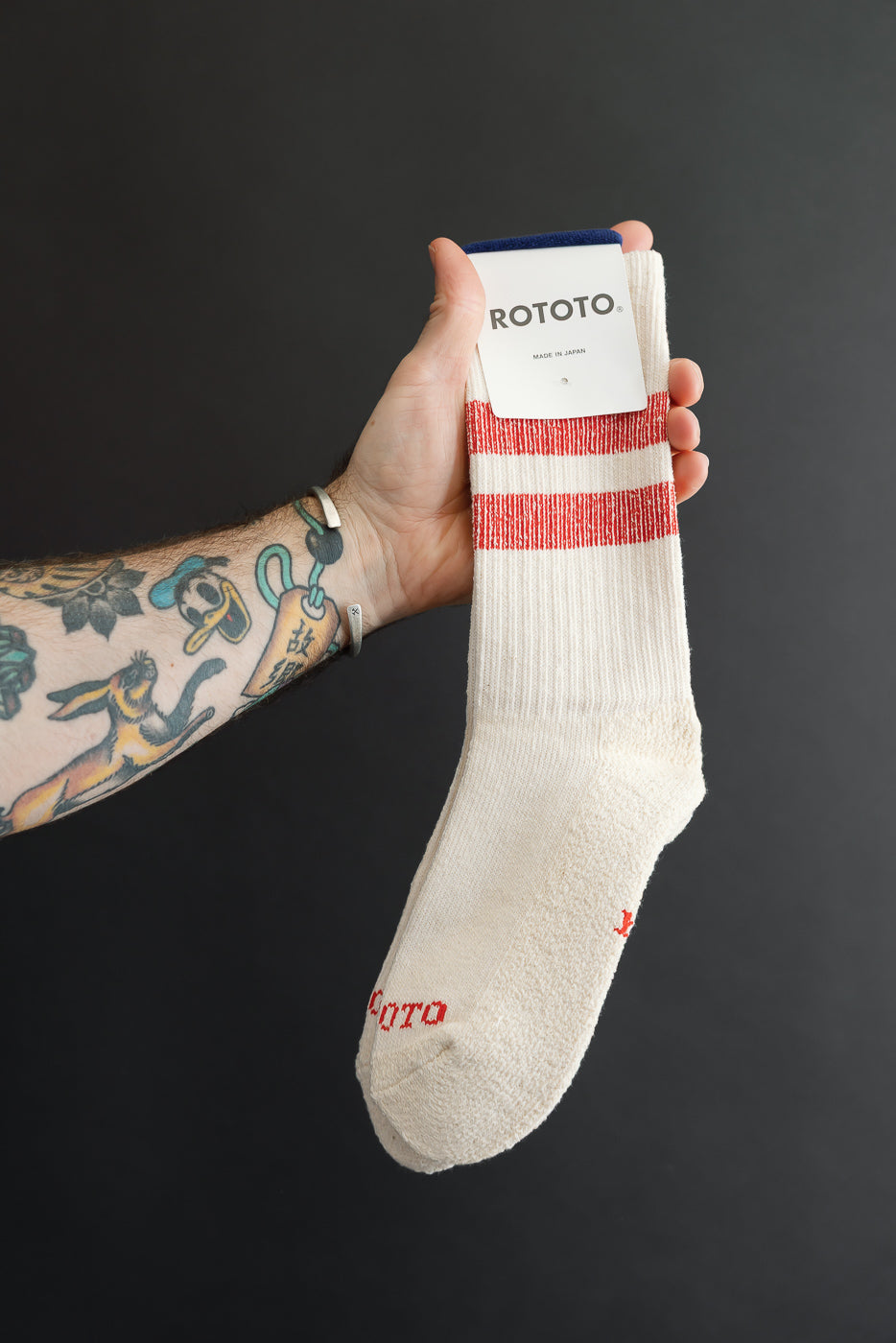 Close-up of the front of a white Rototo sock with red stripes and logo held by a male hand.