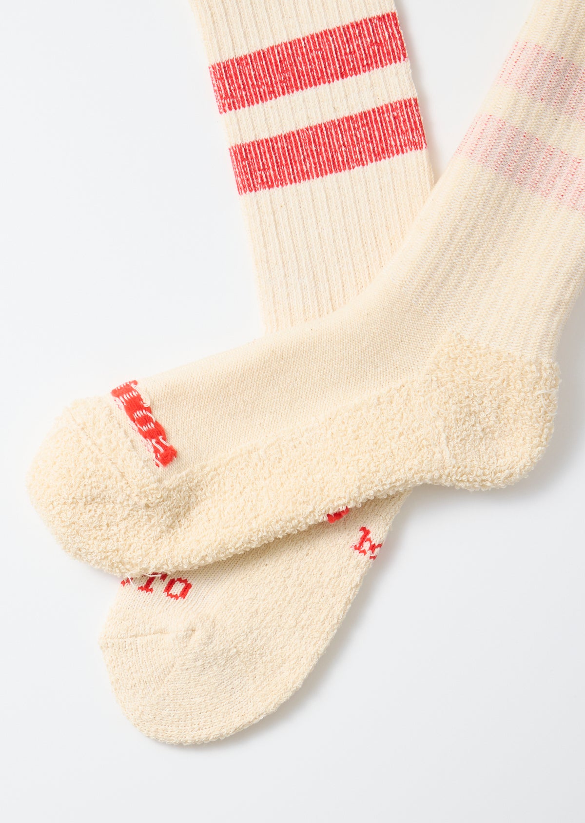 Close-up of the front of cream-colored crew socks with red stripes and text detail.