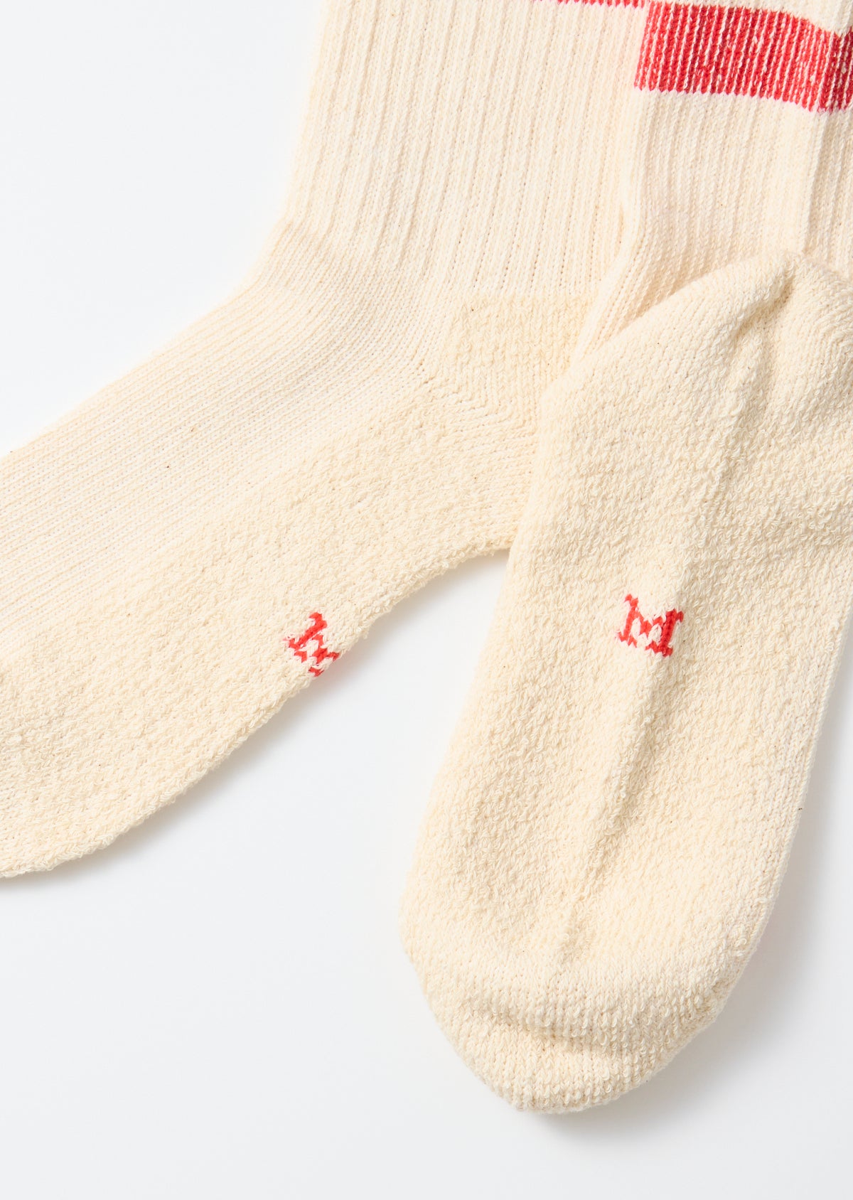Close-up of the toes and soles of cream-colored socks with small red 'M' embroidery.