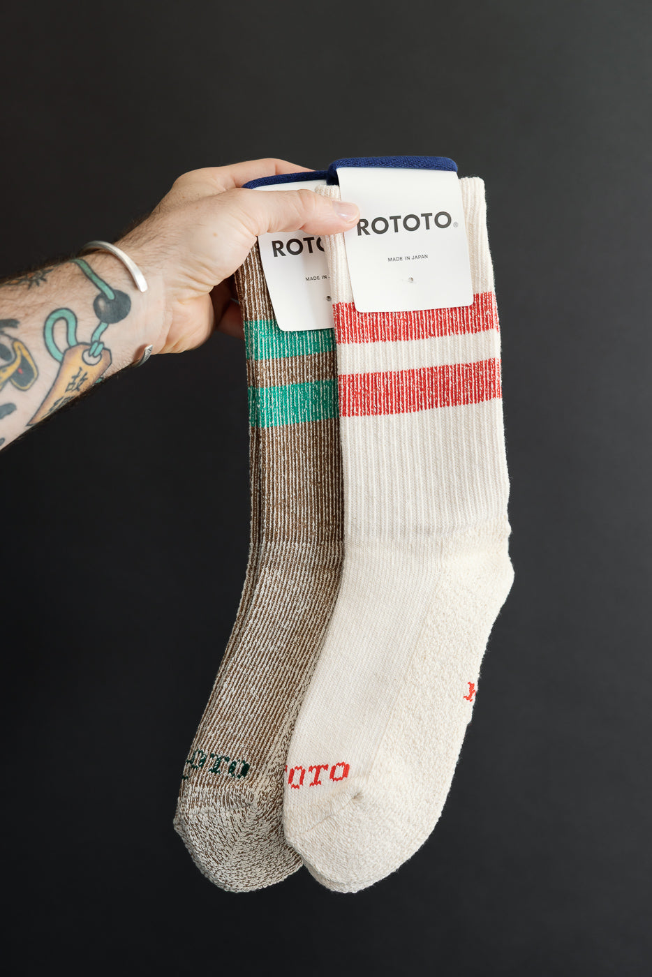 Close-up of front view of two ROTOTO socks: one tan with green stripes and one cream with red stripes.