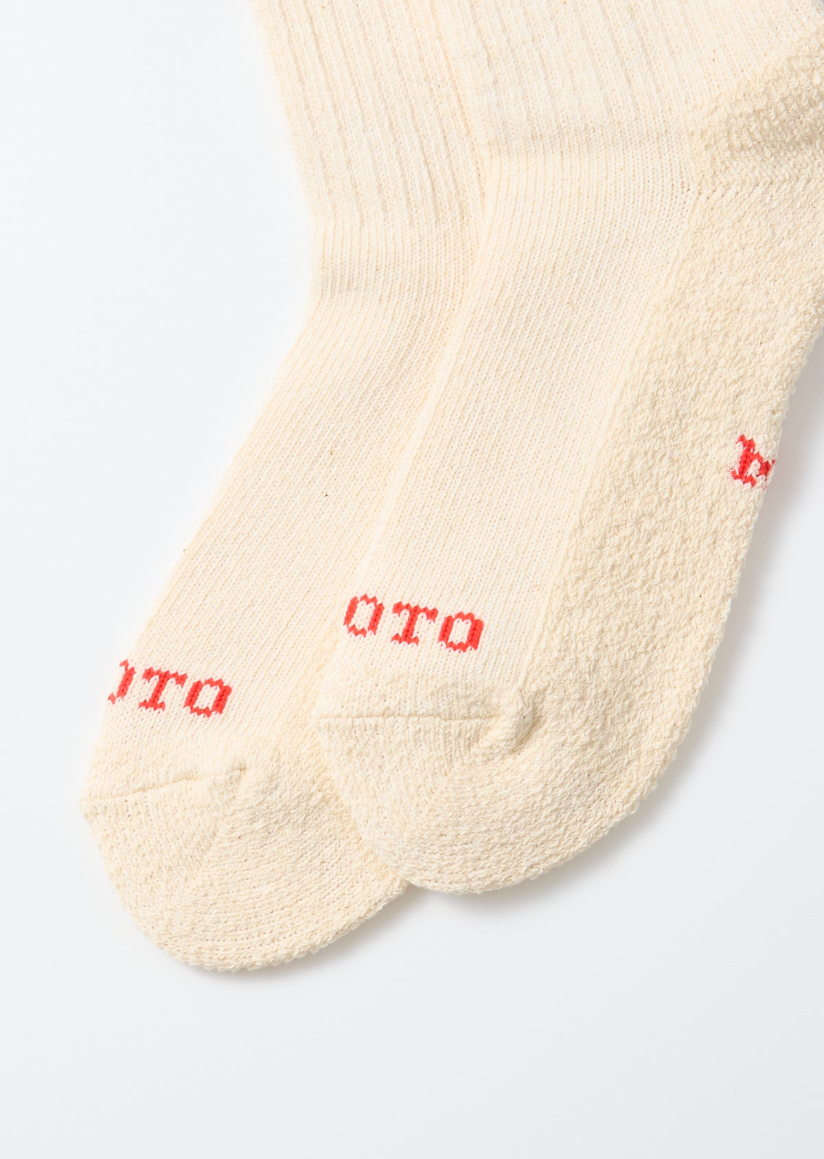 Flat lay close-up of the front of cream ribbed crew socks with red text detail.