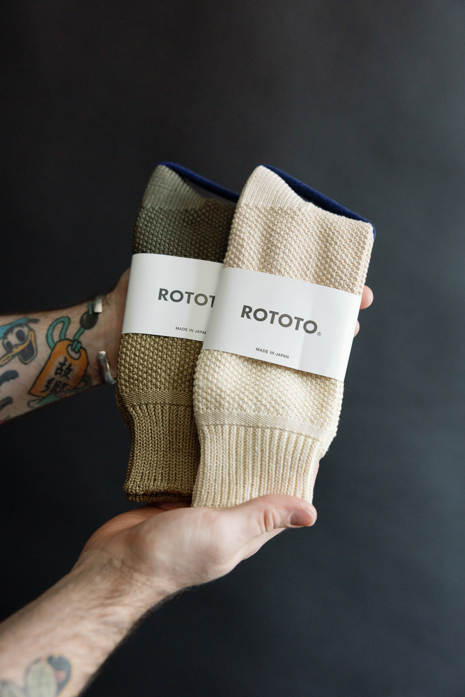 Close-up of male hand holding Rototo seed stitch socks, front view, olive and beige color.