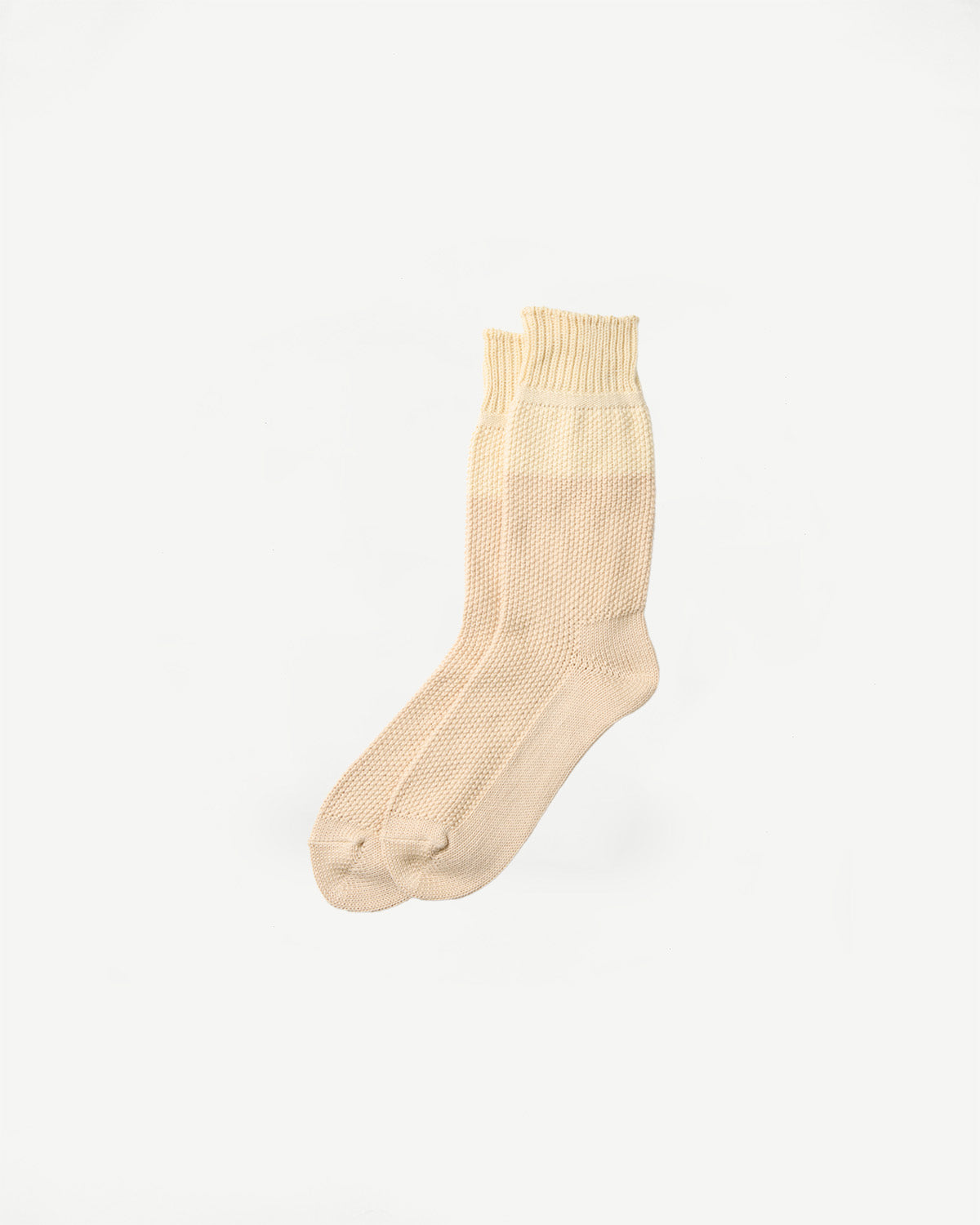 Flat lay of Rototo raw beige seed stitch socks, front view, showing ribbed cuff and textured knit.