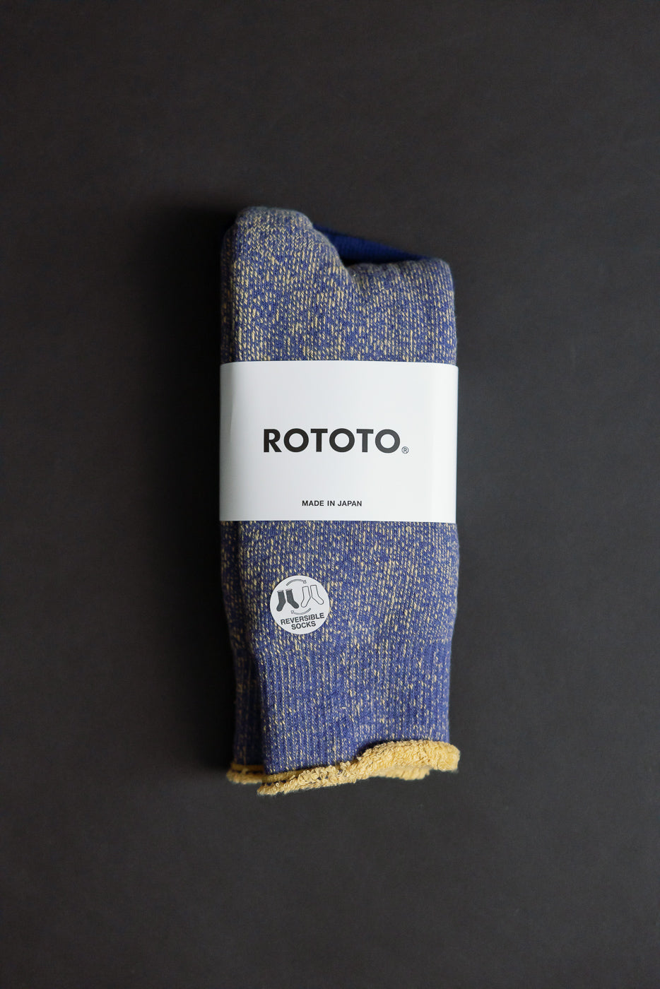 R1612 - Reversible Pile Socks - Blue, Light Yellow, showcasing a speckled knit with contrasting yellow-cream interior, wrapped in a branded ROTOTO paper band, highlighting their reversible design inspired by 1970s college T-shirts.