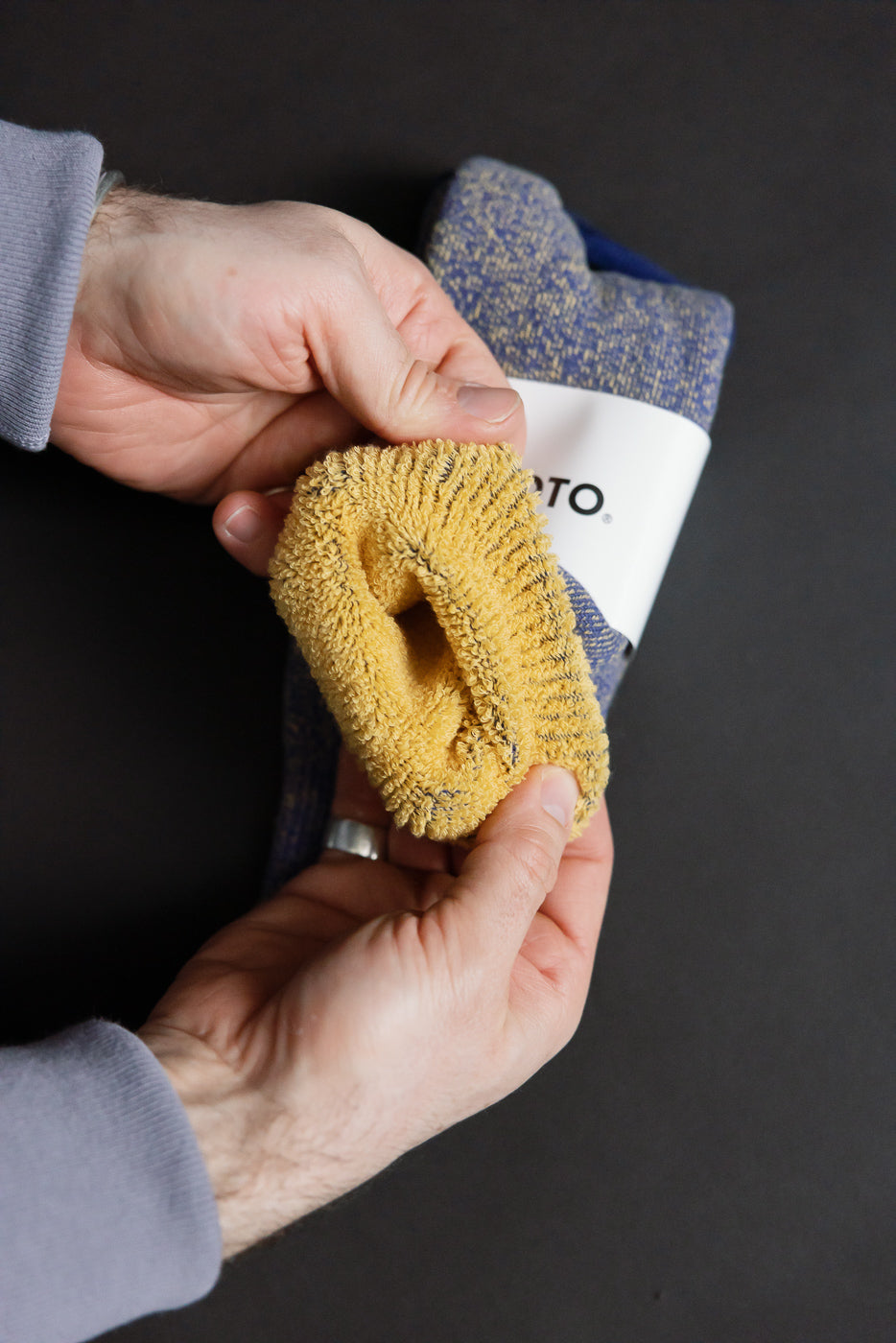 Hands holding R1612 - Reversible Pile Socks, featuring a mustard yellow terry-cloth knit and a blue-gray flecked yarn, showcasing their two-tone reversible design with a soft, dense cotton texture.