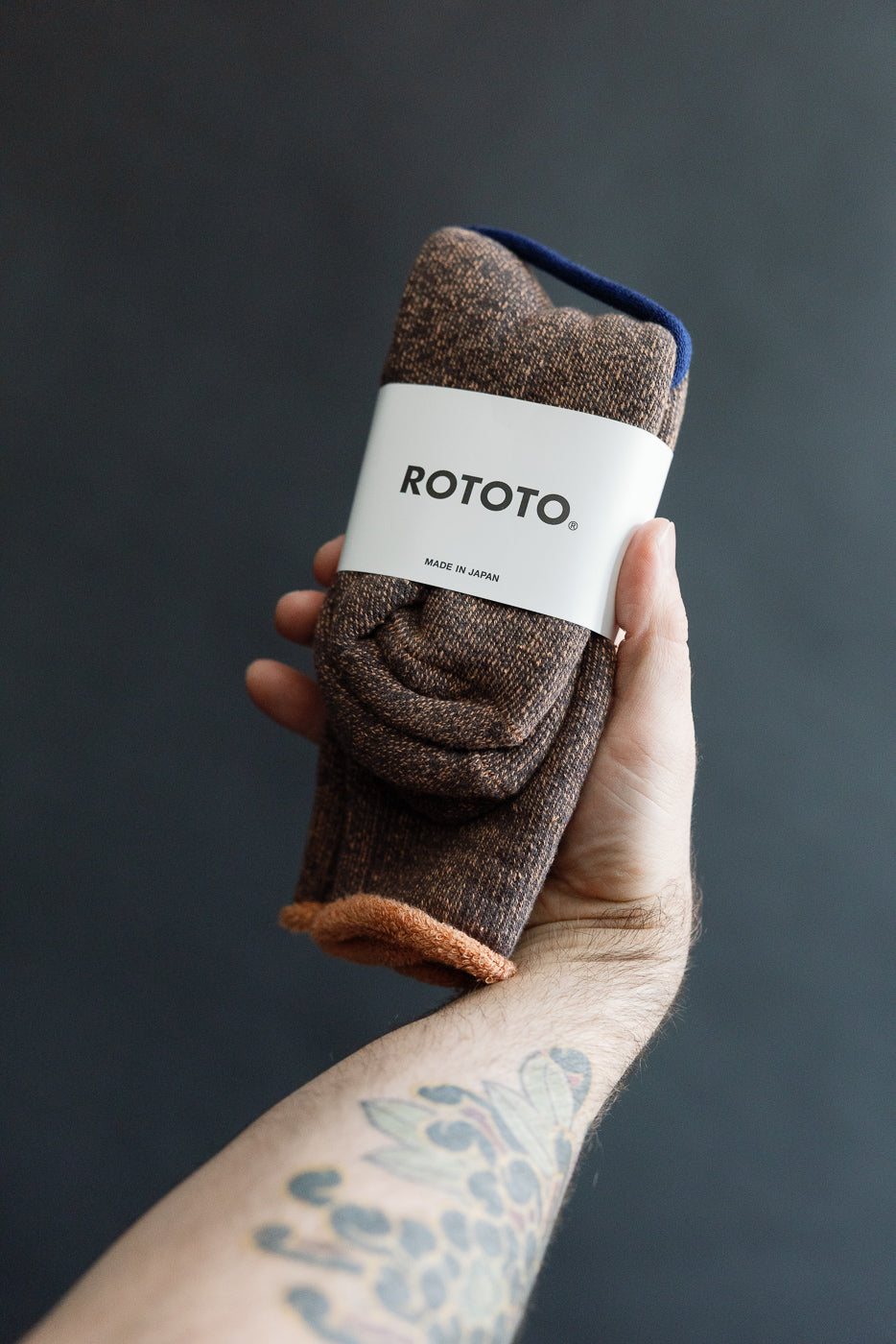 Close-up of ROTOTO reversible pile socks in faded black and light orange, front flat lay, packaging visible, held in hand.