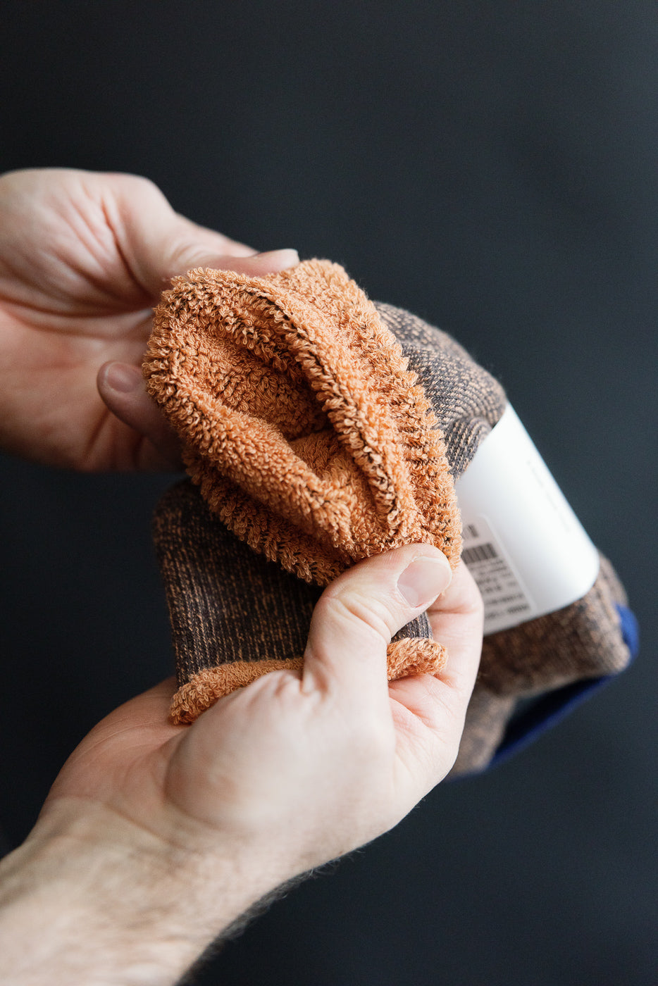 Close-up of Rototo reversible pile socks in faded black and light orange, showing textured interior fabric detail.