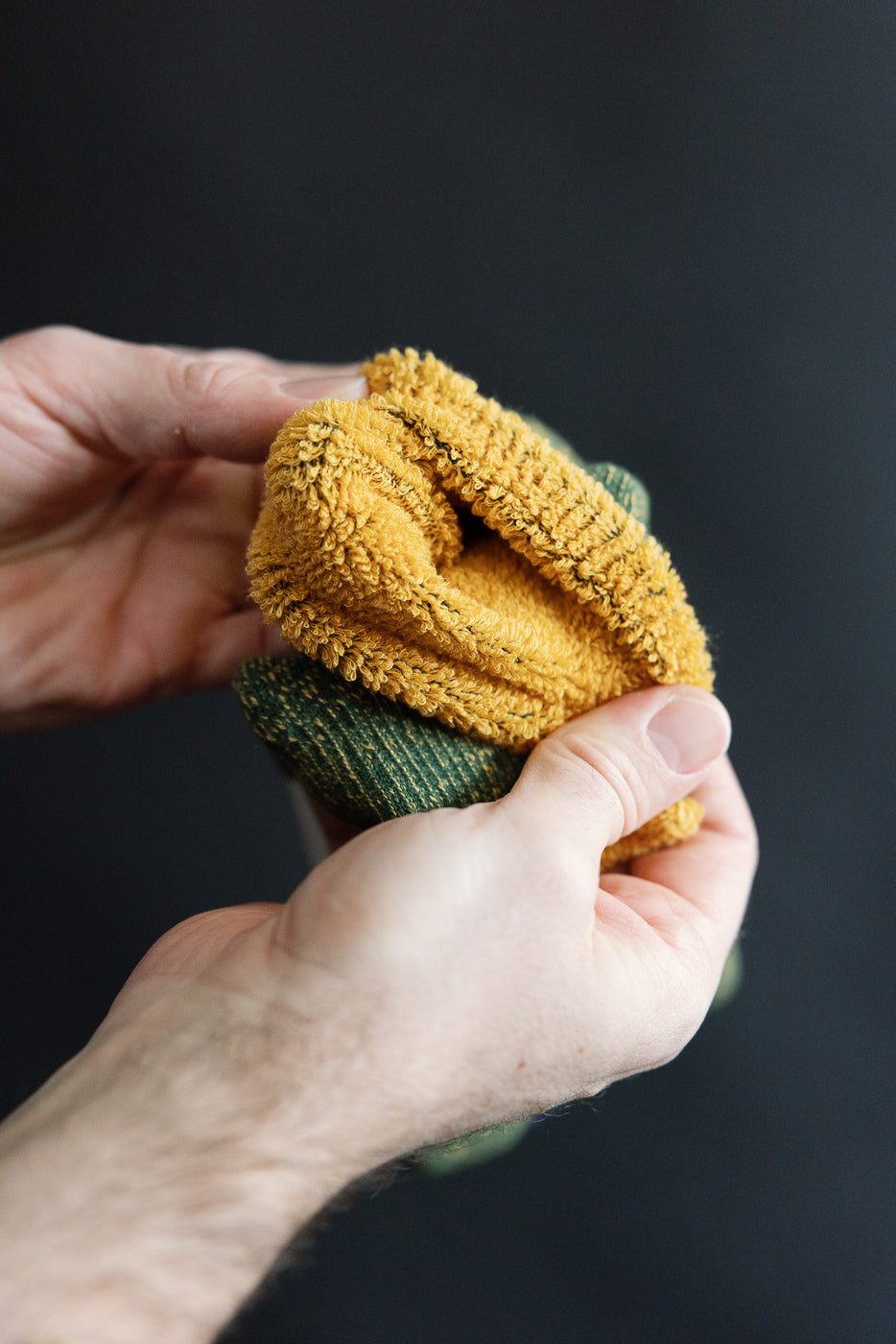 Close-up of hand holding Rototo R1612 reversible pile socks, yellow terry inside, green knit outside