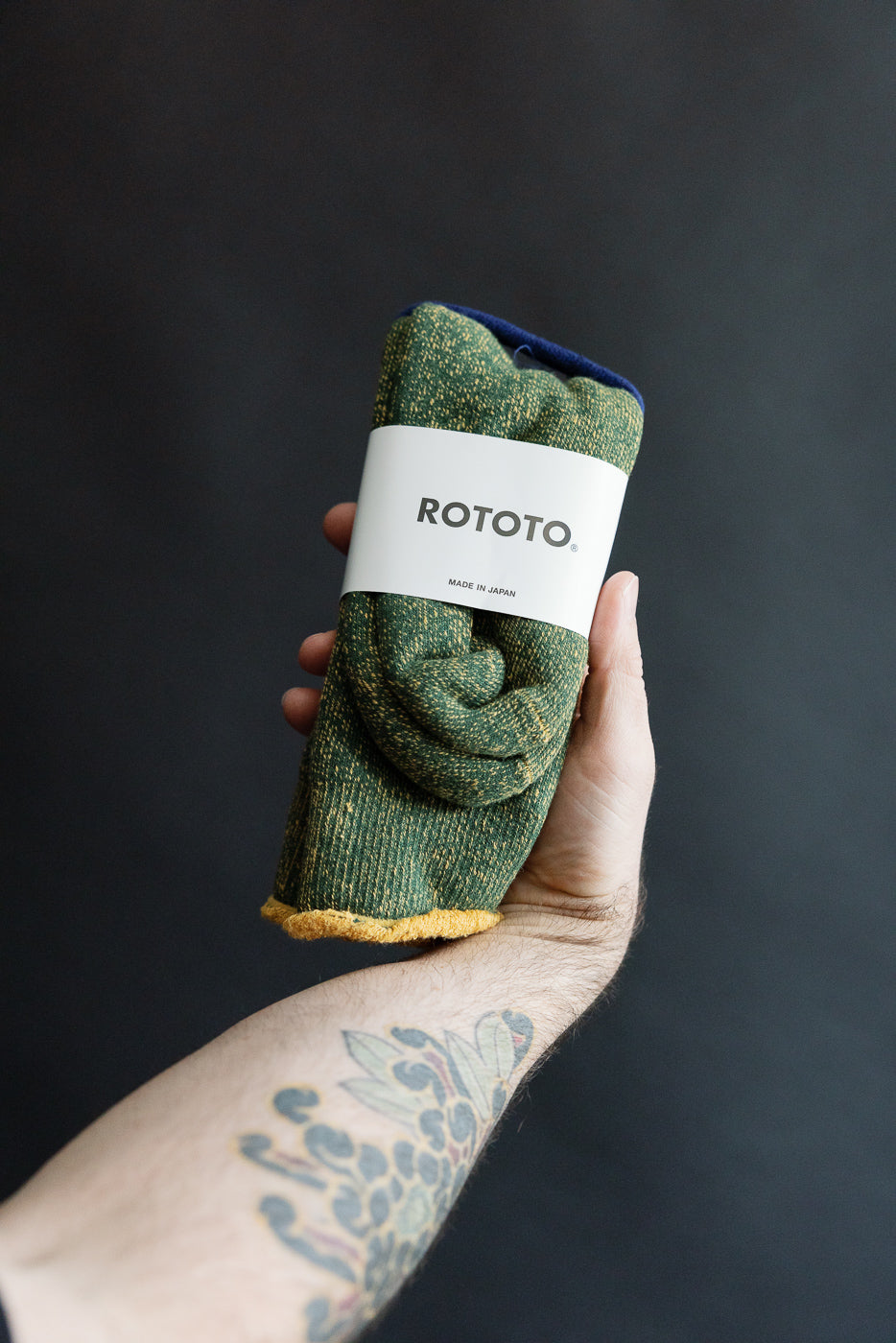 Close-up of hand holding Rototo reversible pile socks, ivy green and dark yellow, with product label.