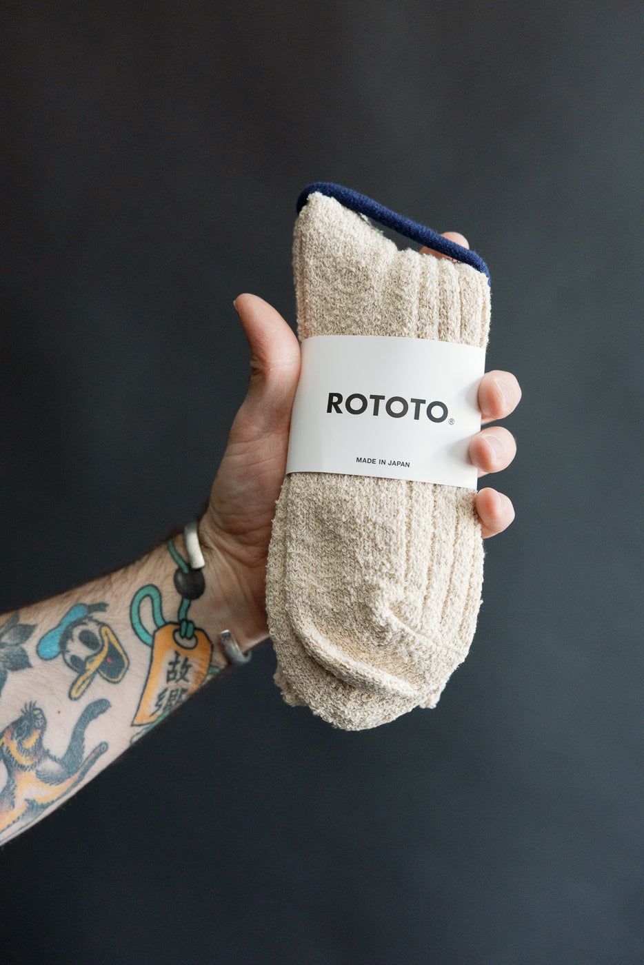 Close-up of a hand holding Rototo recycled cotton boucle crew socks in ecru, front side view.