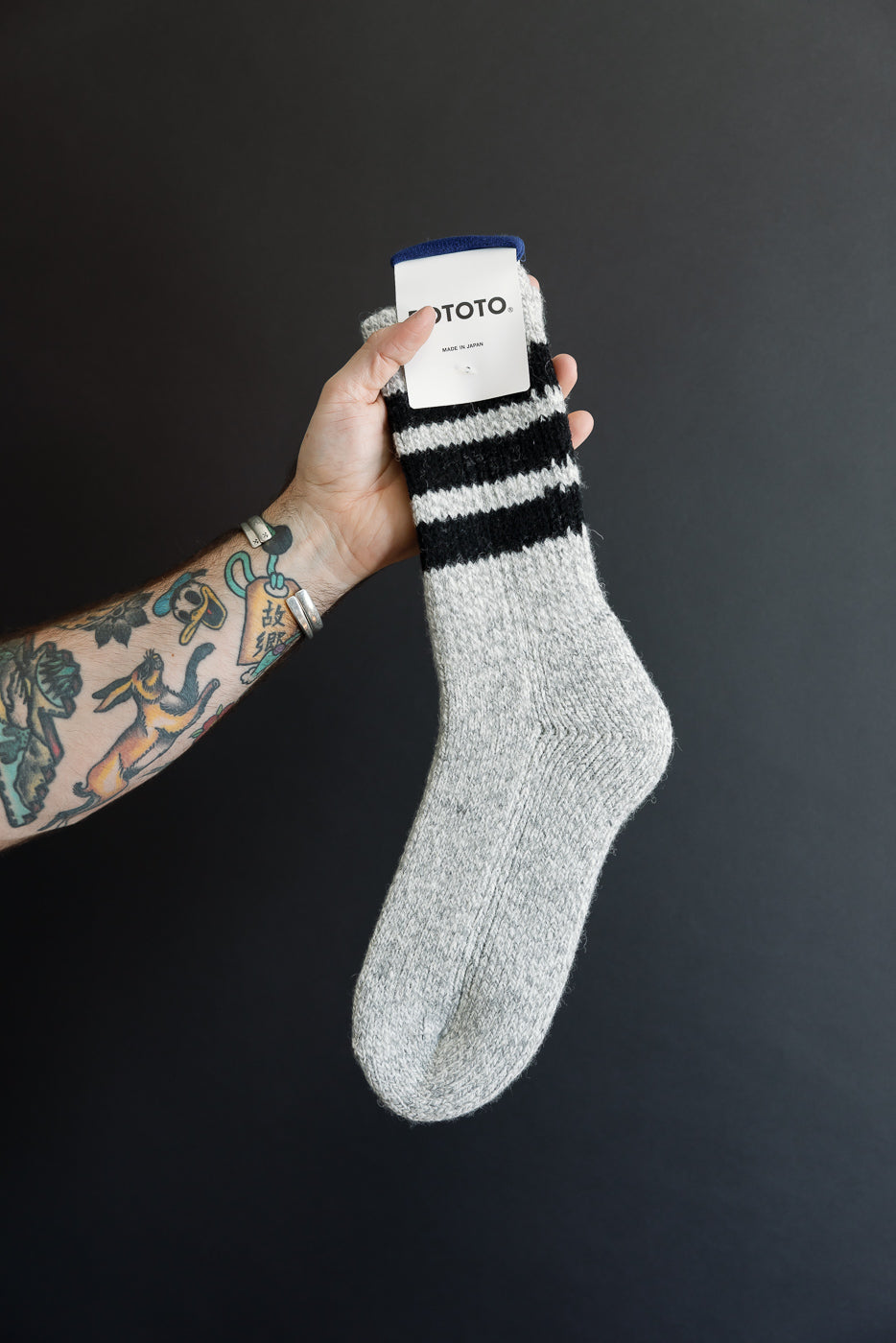 Close-up of the front of a grey marl knit sock with black stripes and a blue cuff.