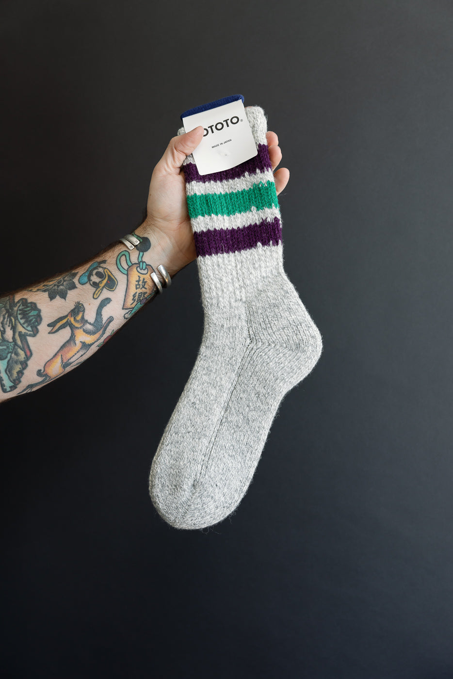 Close-up of the side view of a grey marl knit sock with purple and green stripes.