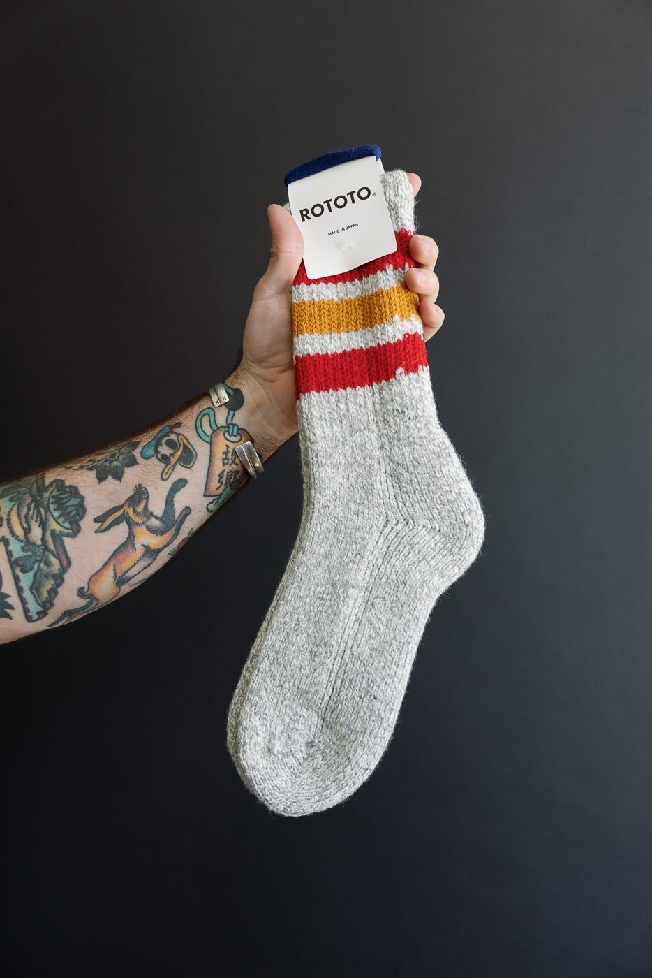 Close-up of the front of a grey ROTOTO sock with red and yellow stripes and a white tag.