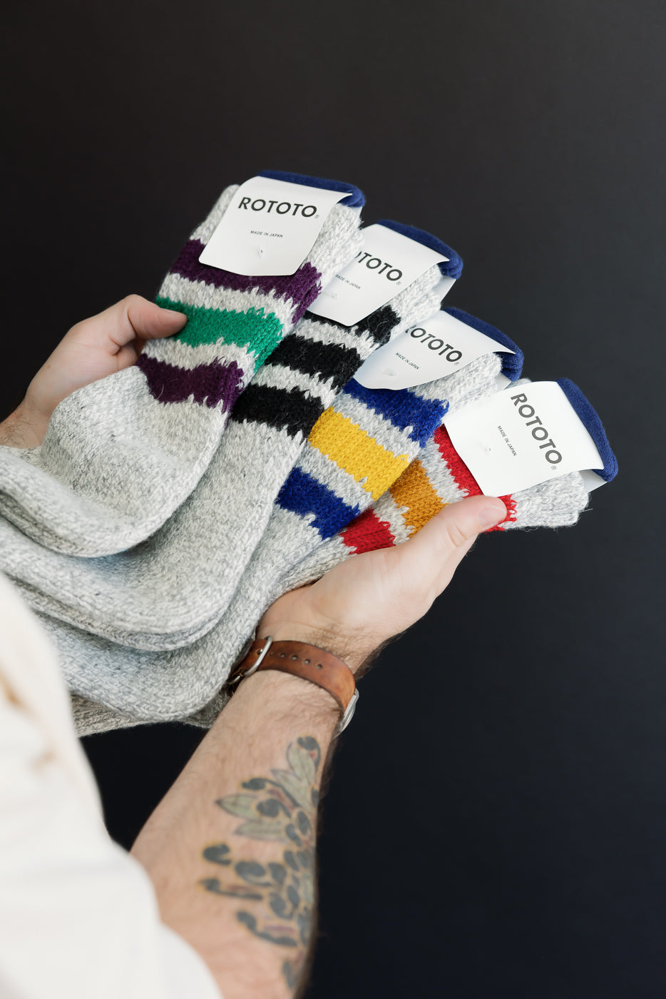 Close-up of a person holding multiple pairs of patterned knit socks with various stripe colors.
