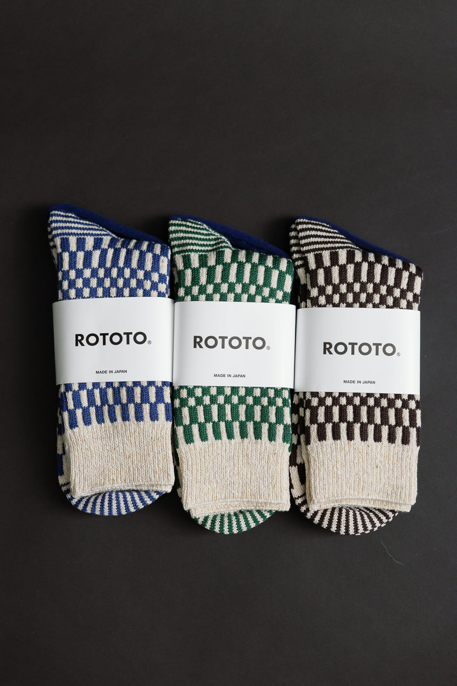 Flat lay close-up of three pairs of checkerboard crew socks, front view, in blue, green, and brown.