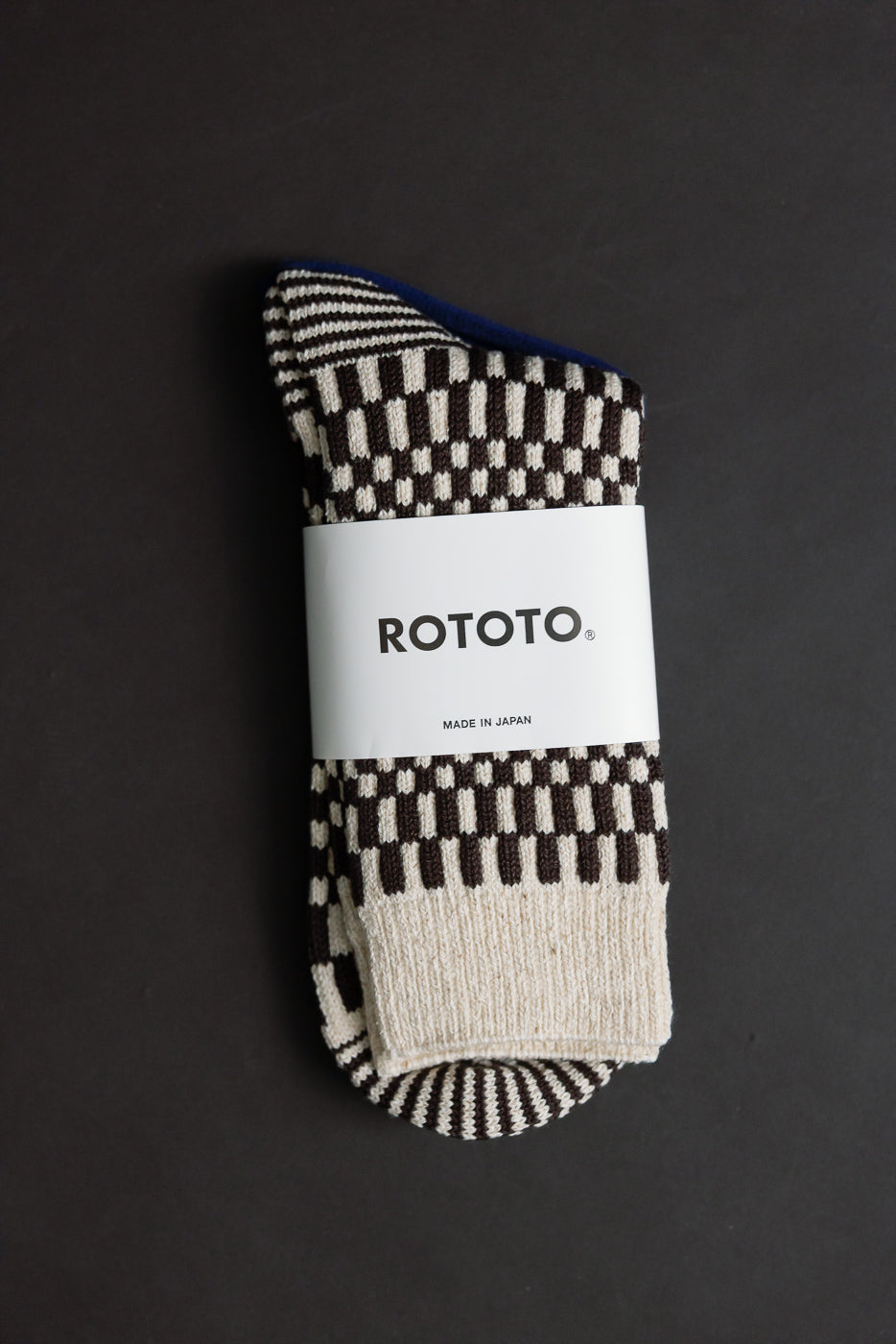 Close-up flat lay of front side of brown checkerboard knit crew socks, packaging visible.