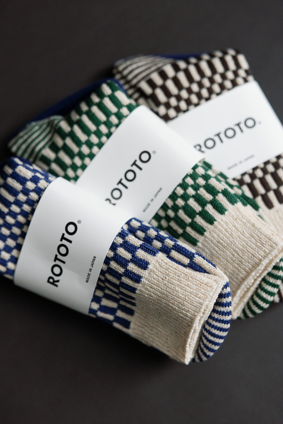 Flat lay close-up of front side of checkerboard pattern crew socks in blue, green, and brown, showing knit texture and packaging.