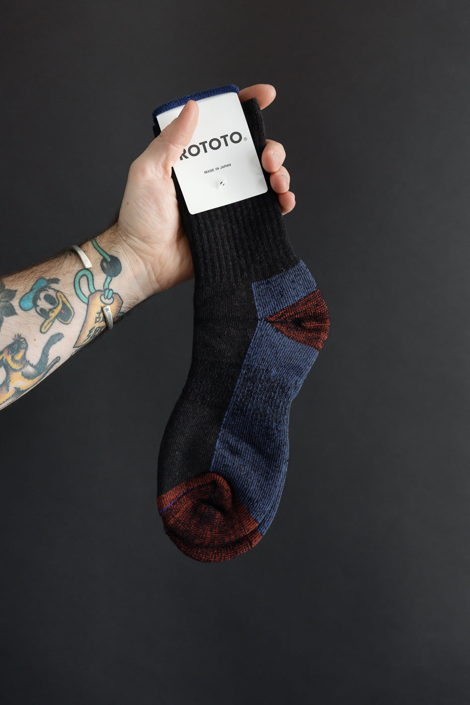 Close-up of a male hand holding a Rototo sock, showing the side view and tag.