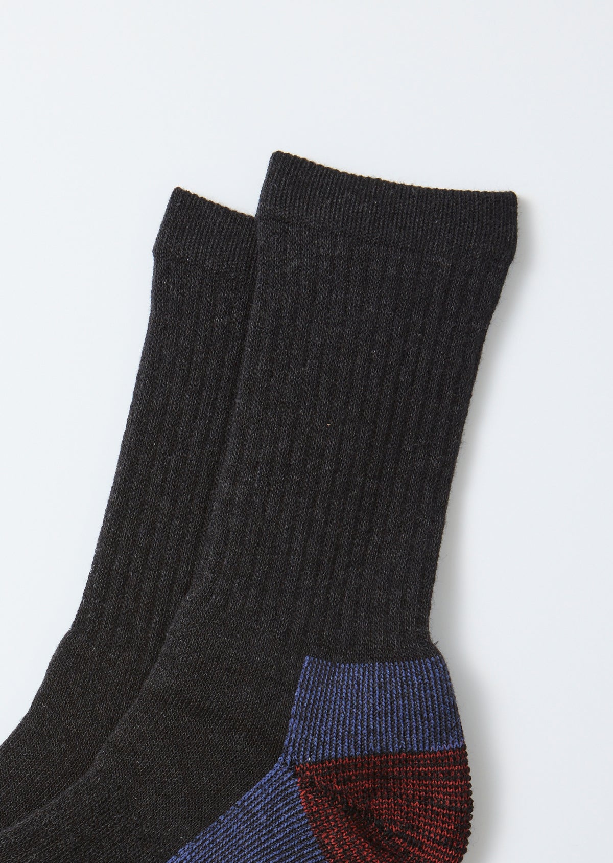 Close-up flat lay of the heel area of dark charcoal ribbed crew socks with blue and red accents.