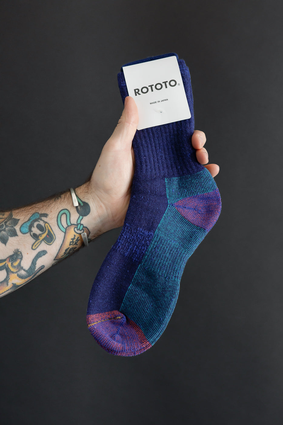 Close-up of the front of a Rototo blue patterned knit sock held by a hand.