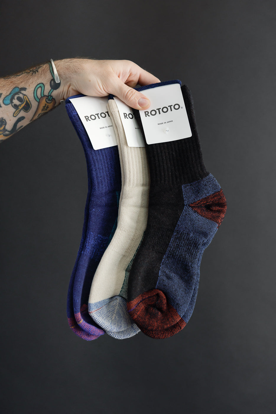 Front view close-up of three pairs of Rototo patterned crew socks in blue, cream, and black.