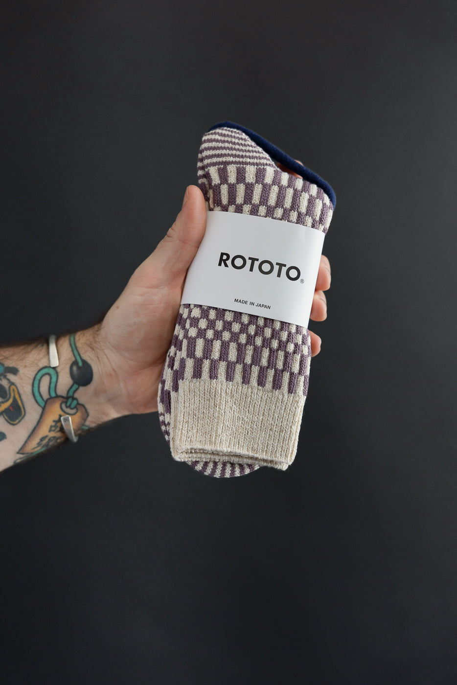 Close-up of the front of a pair of patterned Rototo socks held by a male hand.