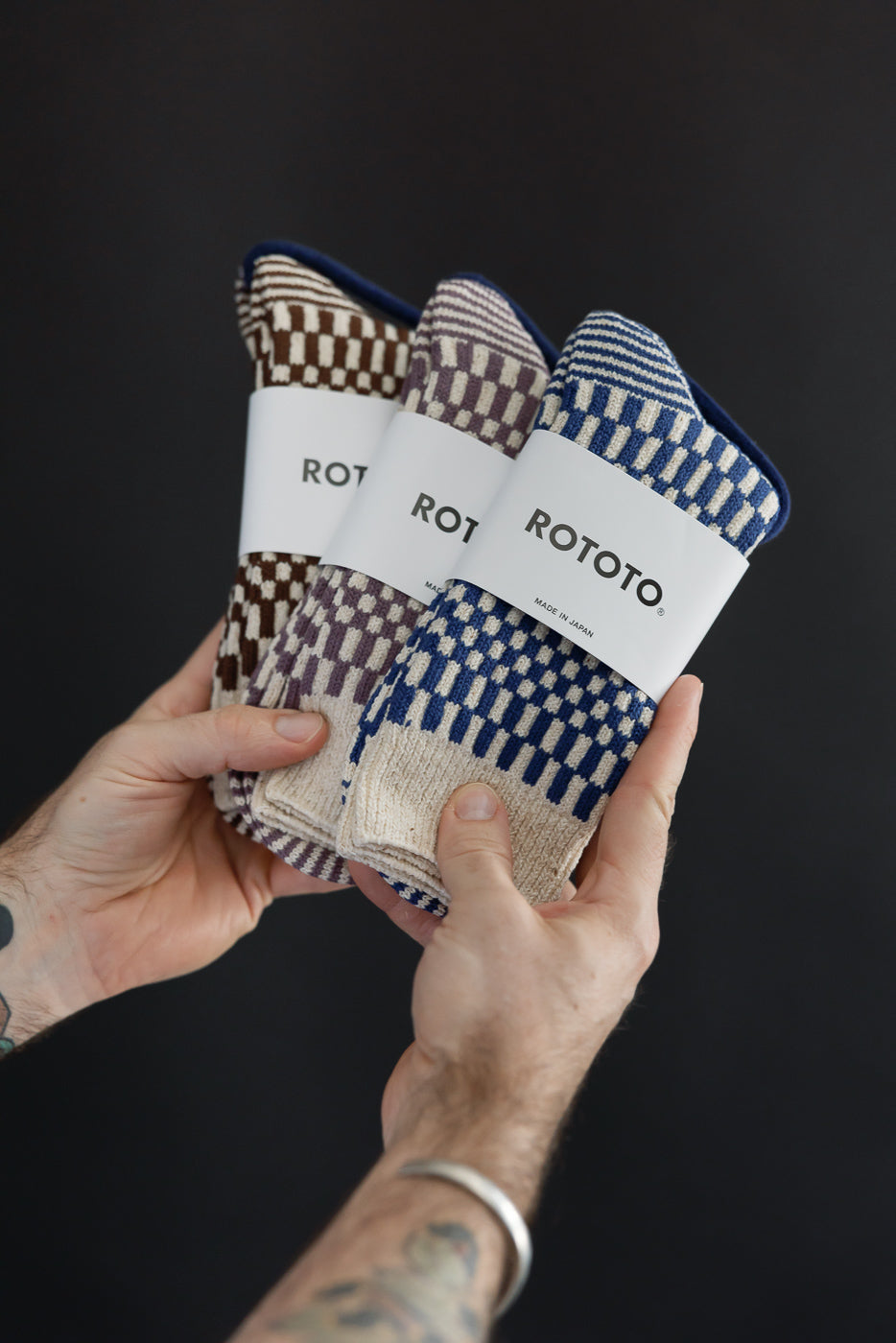 Close-up of three pairs of patterned ROTOTO socks held by male hands.