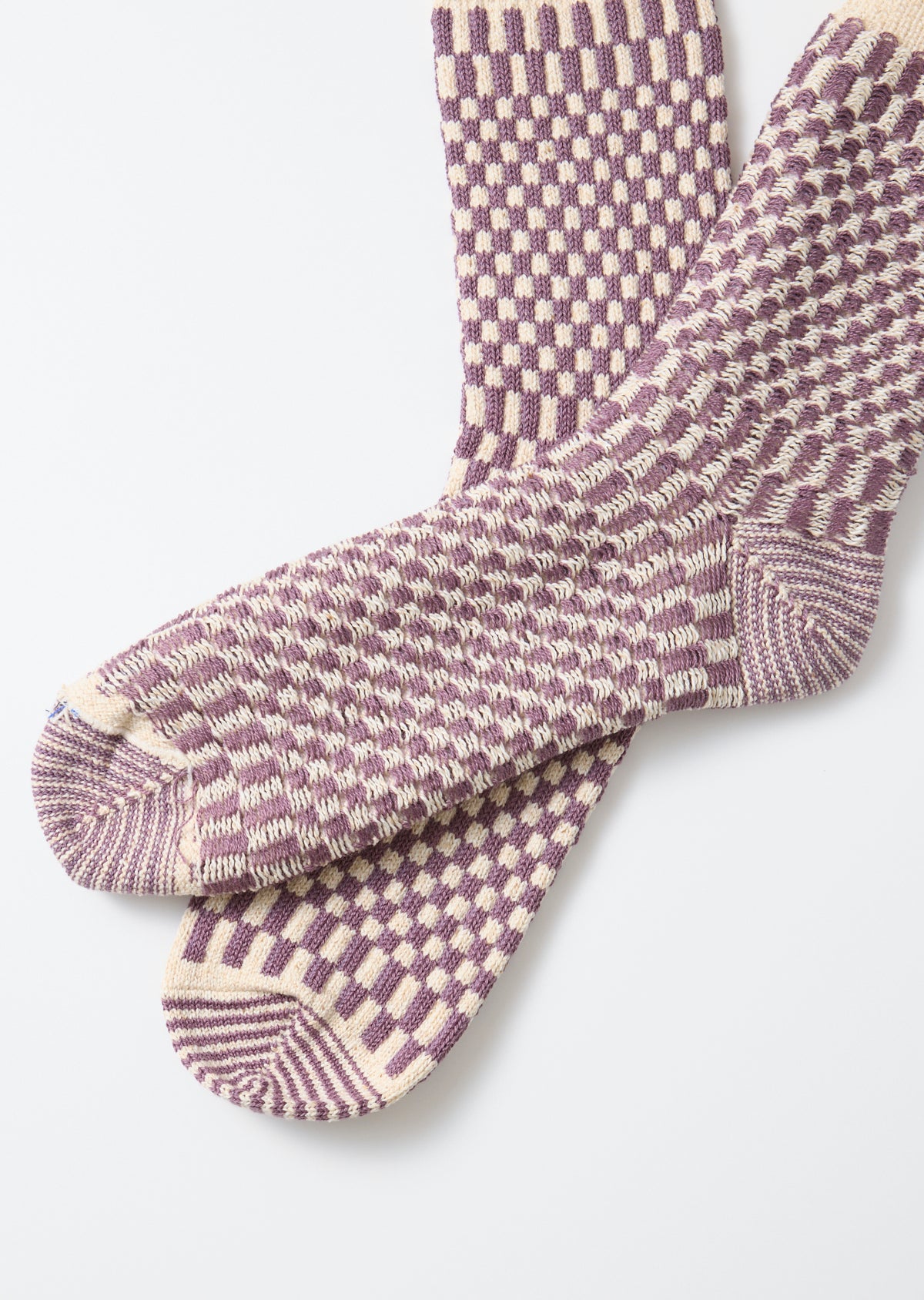 Flat lay close-up of the front side of purple and cream checkered knit crew socks.