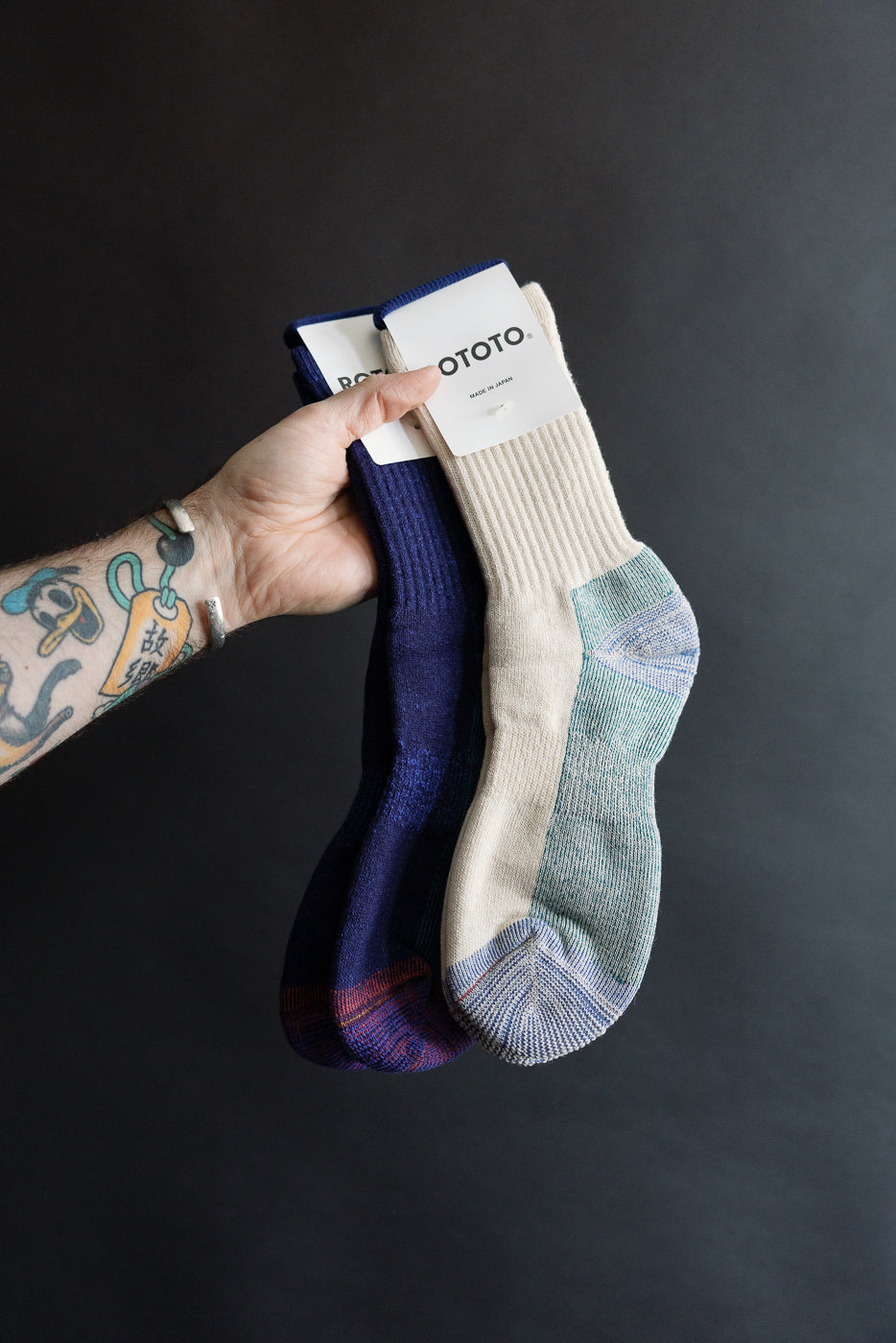 Close-up front view of ROTOTO double face merino pile socks in natural and navy, held by hand, showing ribbed cuff and contrasting heel and toe details.