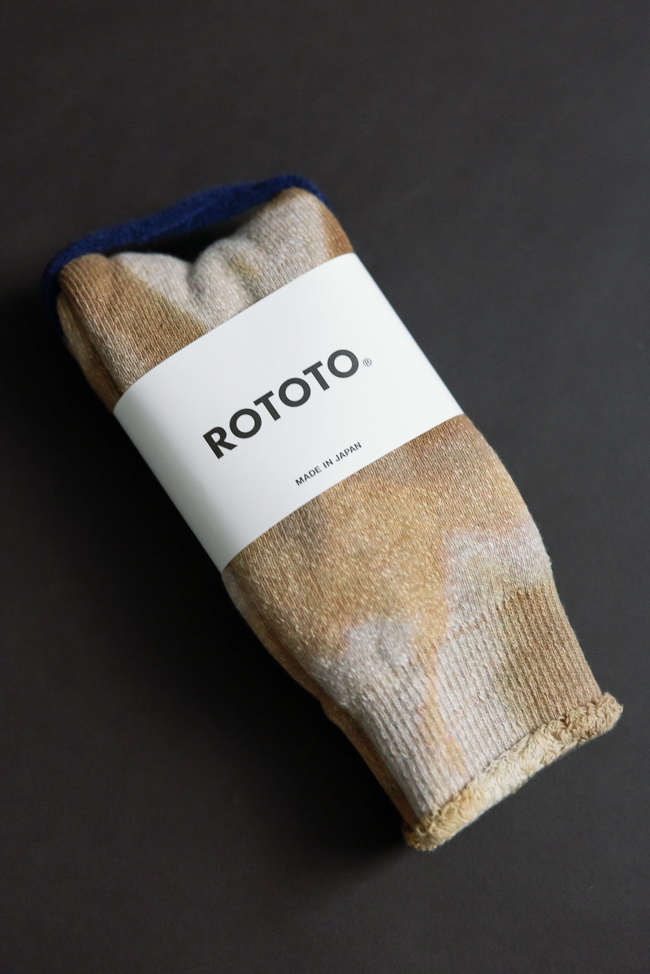 Close-up front view of beige brown tie-dye crew socks, folded with product label visible