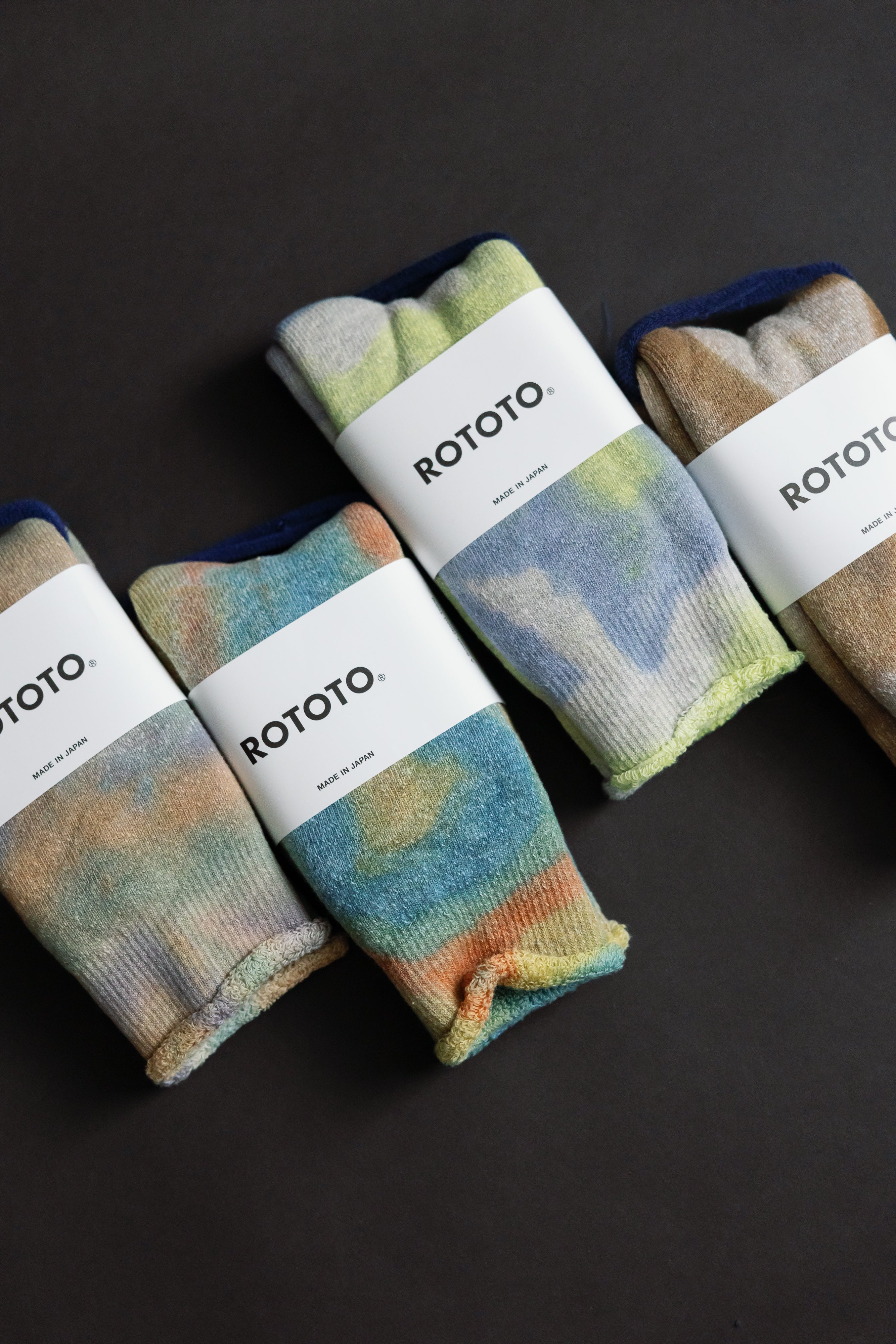 Flat lay front view of four pairs tie-dye crew socks in green, light pink, purple tones, folded.