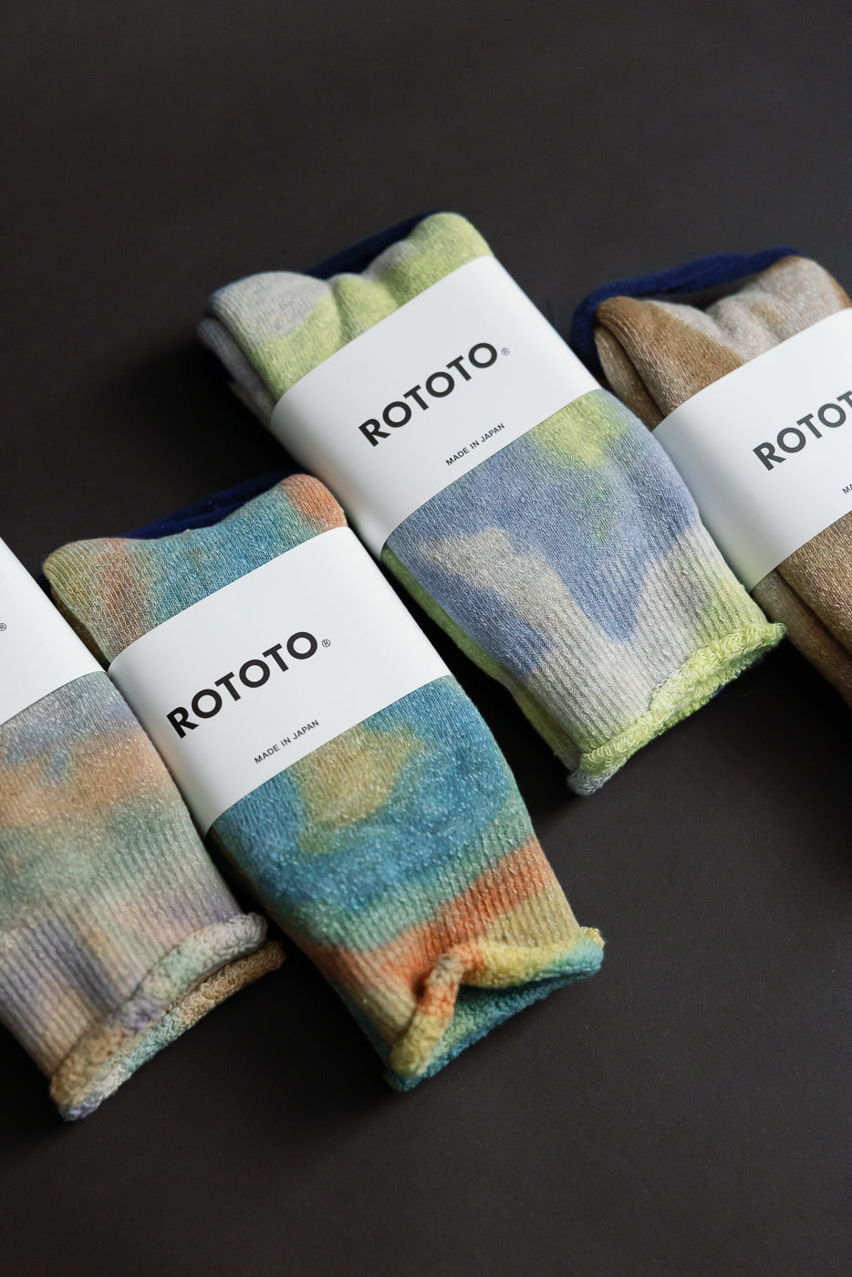 Close-up flat lay of the front side of tie-dye crew socks in pastel green, pink, and purple hues with packaging label visible.