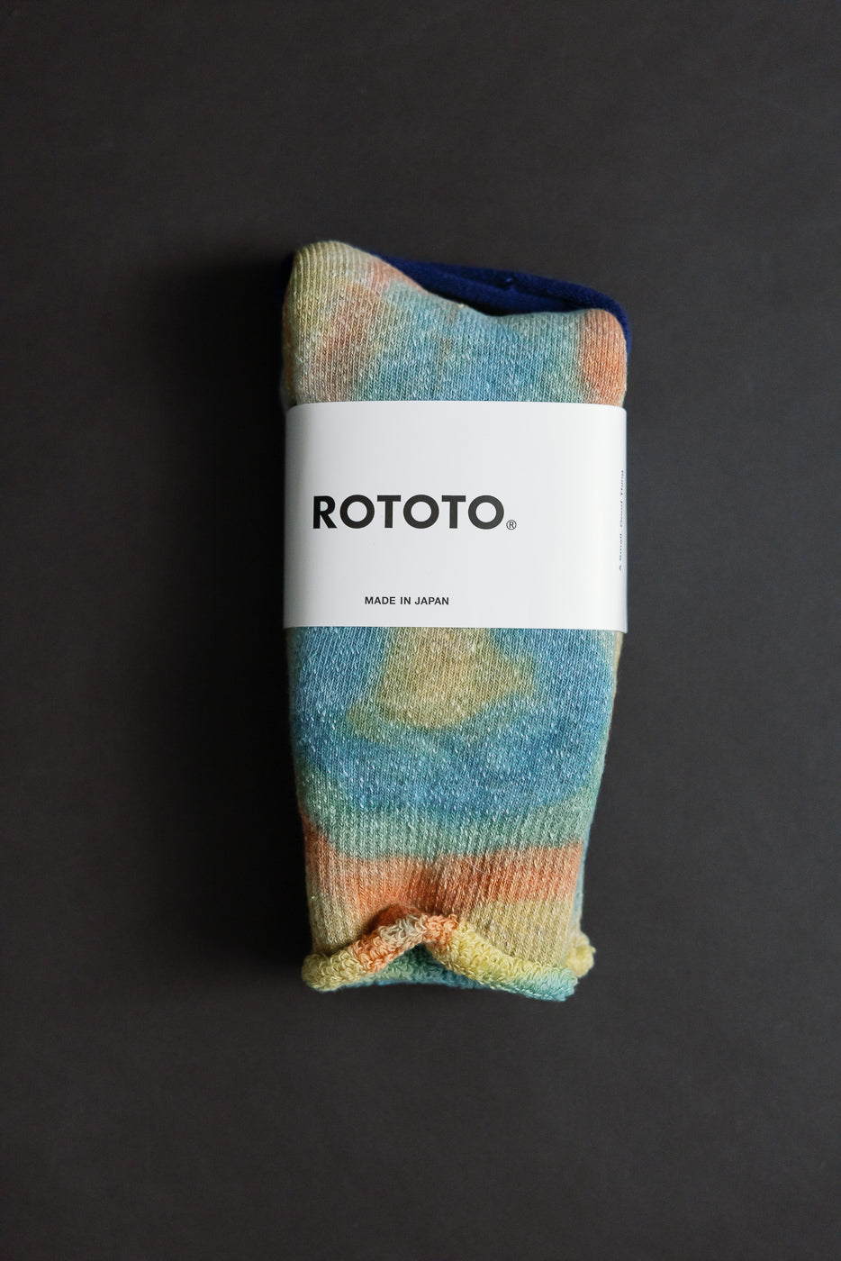 Close-up flat lay of front side of tie-dye crew socks in orange, blue, and yellow tones, packaged.