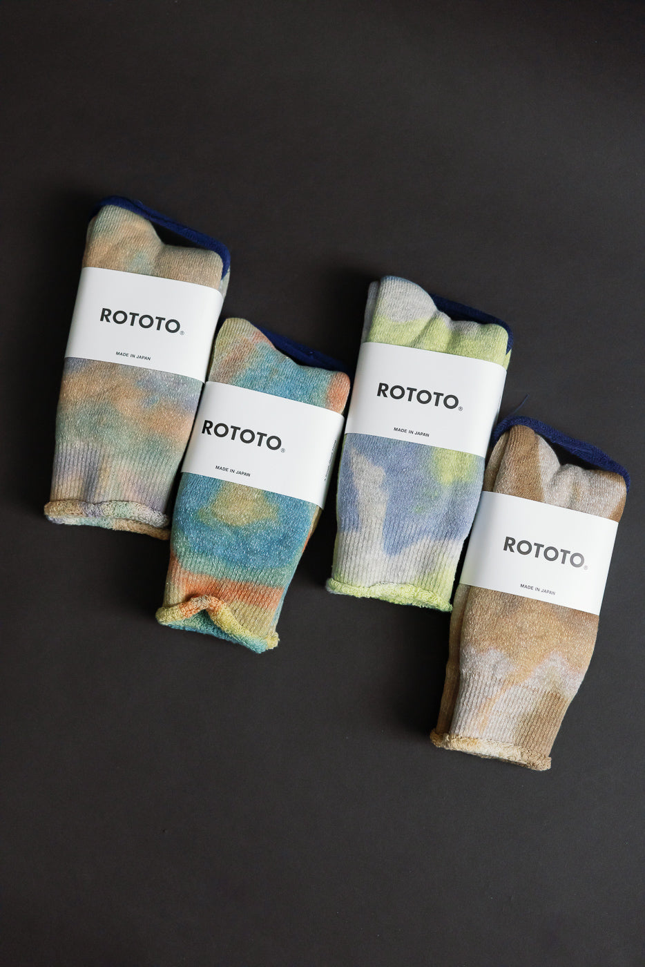 Flat lay front view of tie-dye crew socks in orange, blue, yellow, and green in packaging.