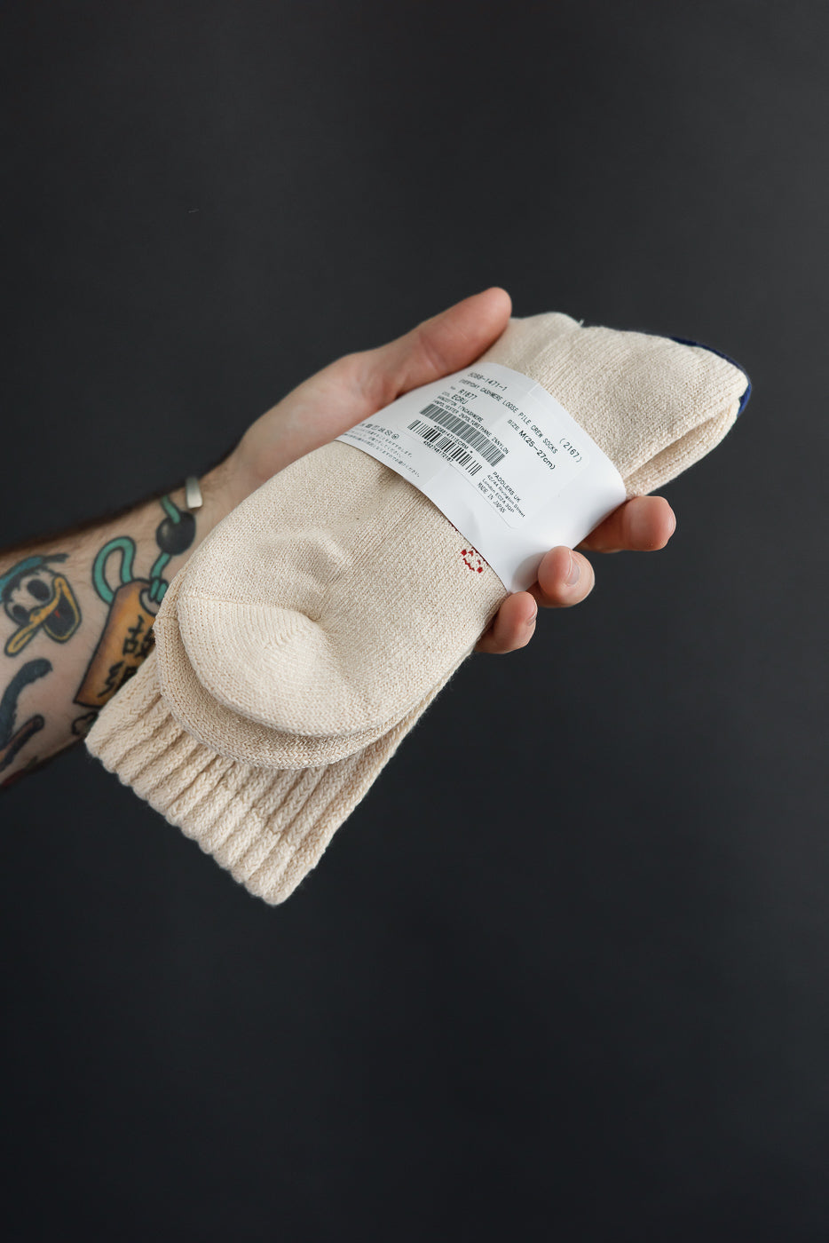 Close-up of the front side of cream ribbed knit socks held in a hand against a black background.