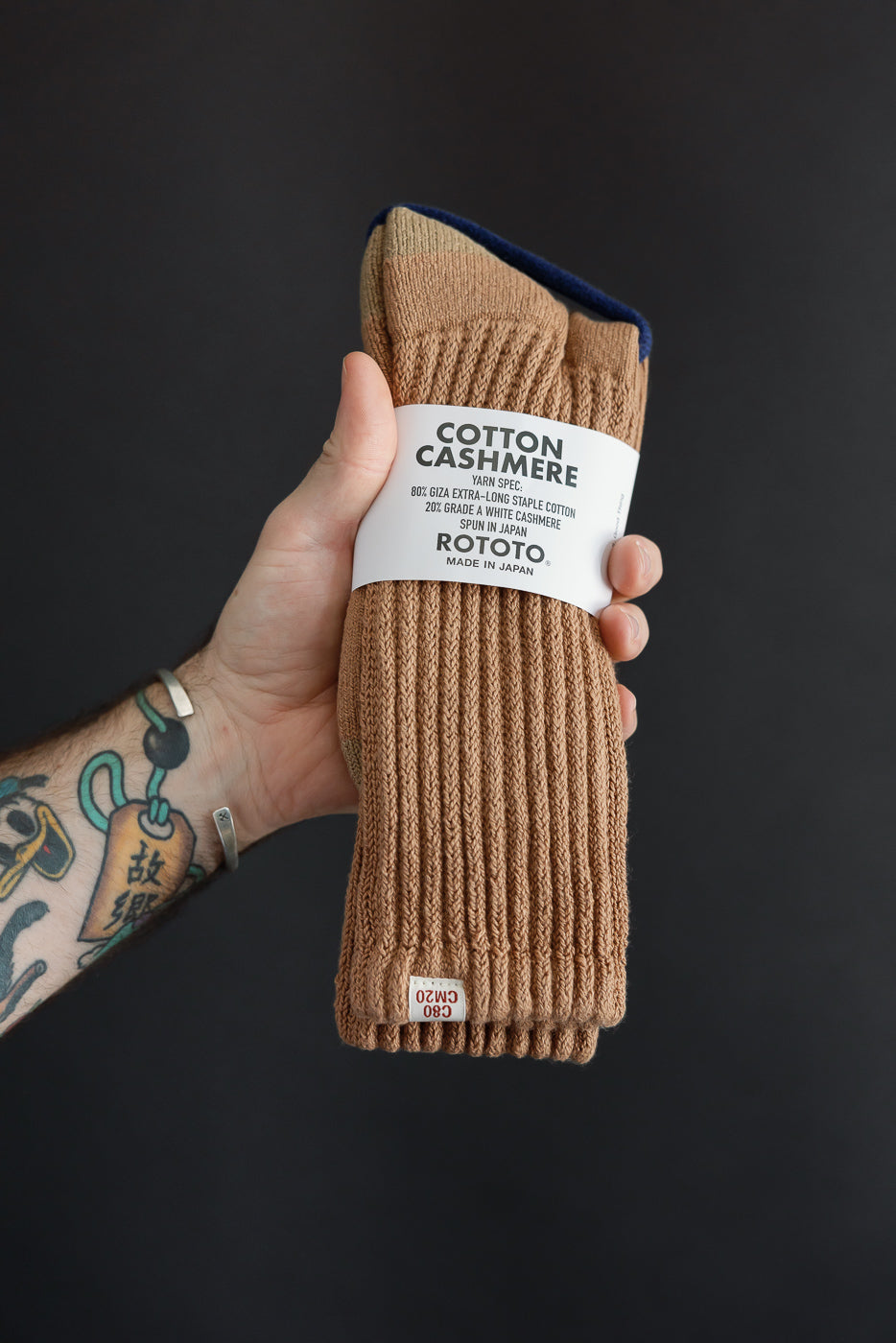 Close-up of the front of a pair of tan ribbed cotton cashmere socks by Rototo held by a man's hand.