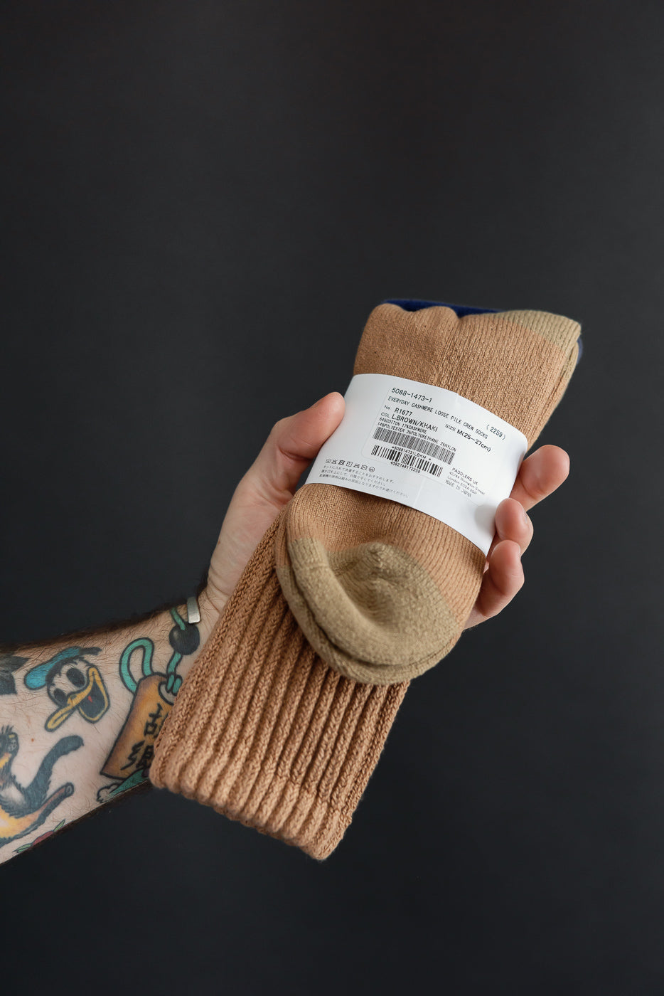 Close-up of a hand holding a pair of tan cashmere blend socks with a white product tag.