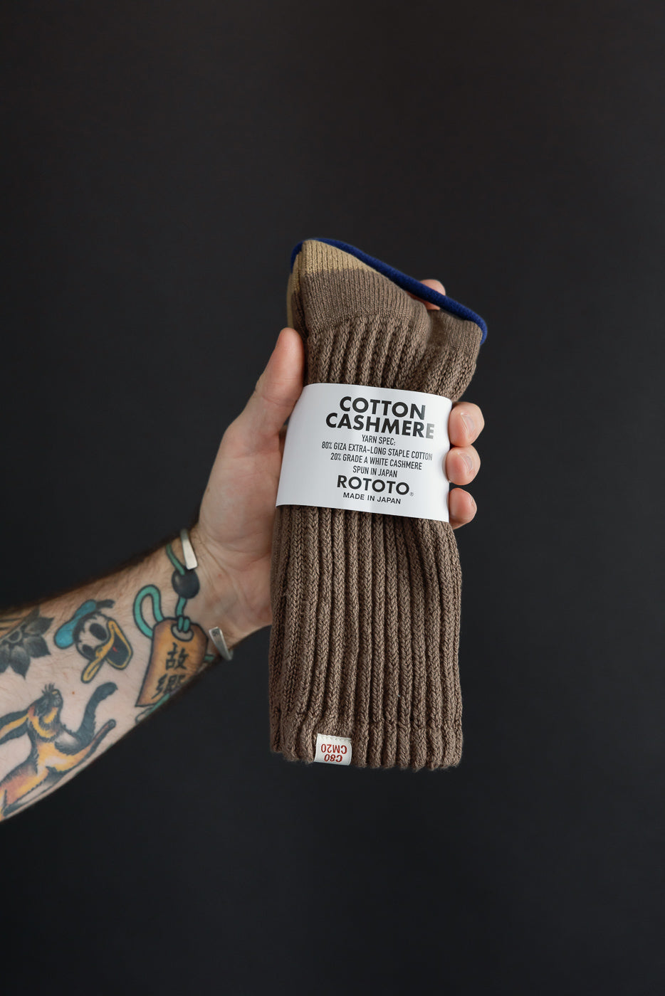 Close-up of the front of a pair of brown ribbed cotton cashmere socks by ROTOTO held by a male hand.