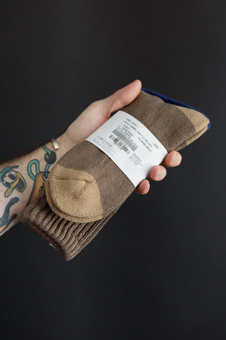 Close-up of a male hand holding brown patterned socks, showing the fabric and tag details.