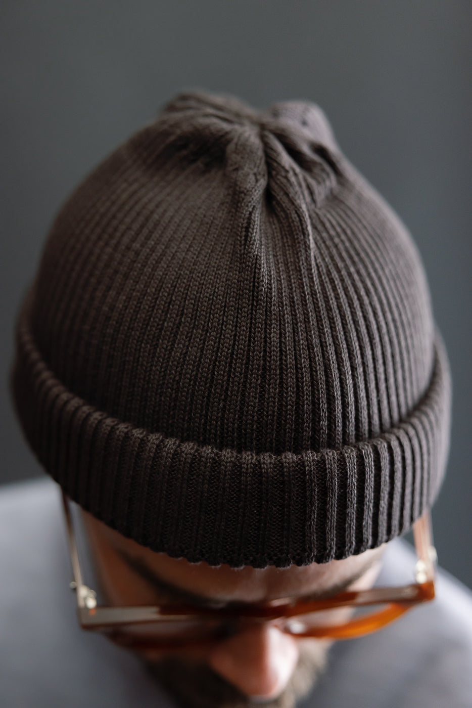 Close-up of dark brown cotton roll-up beanie, top and front detail, worn by male model 5'9