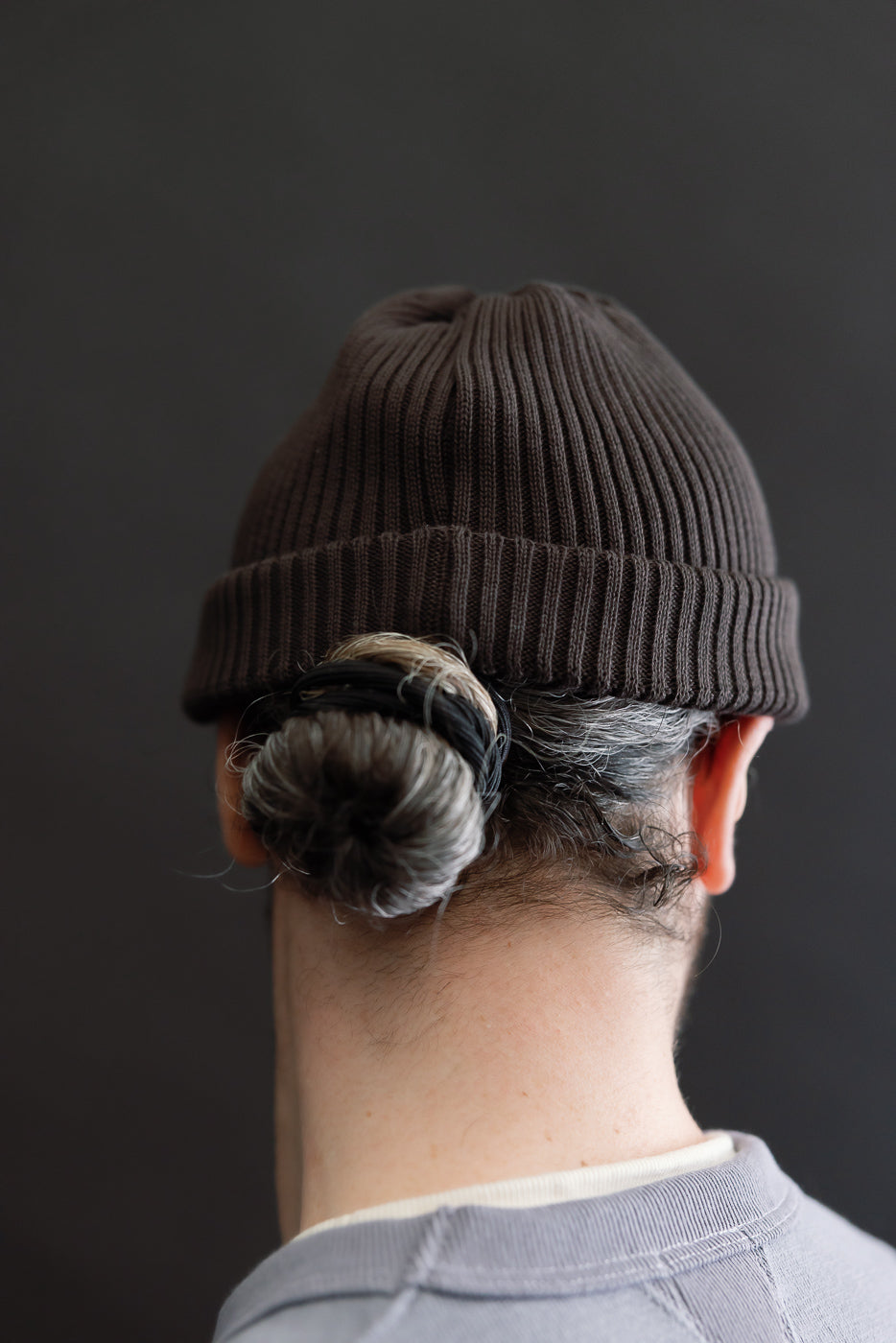 Close-up rear view of dark brown cotton roll-up beanie on male model, showing back fit.