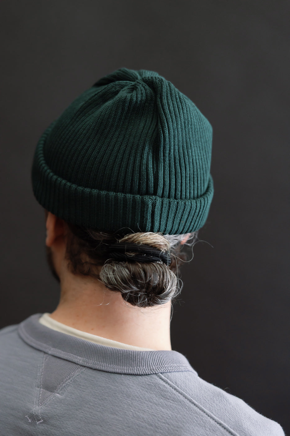 Back view close-up of forest green ribbed cotton beanie on male model, 5'9
